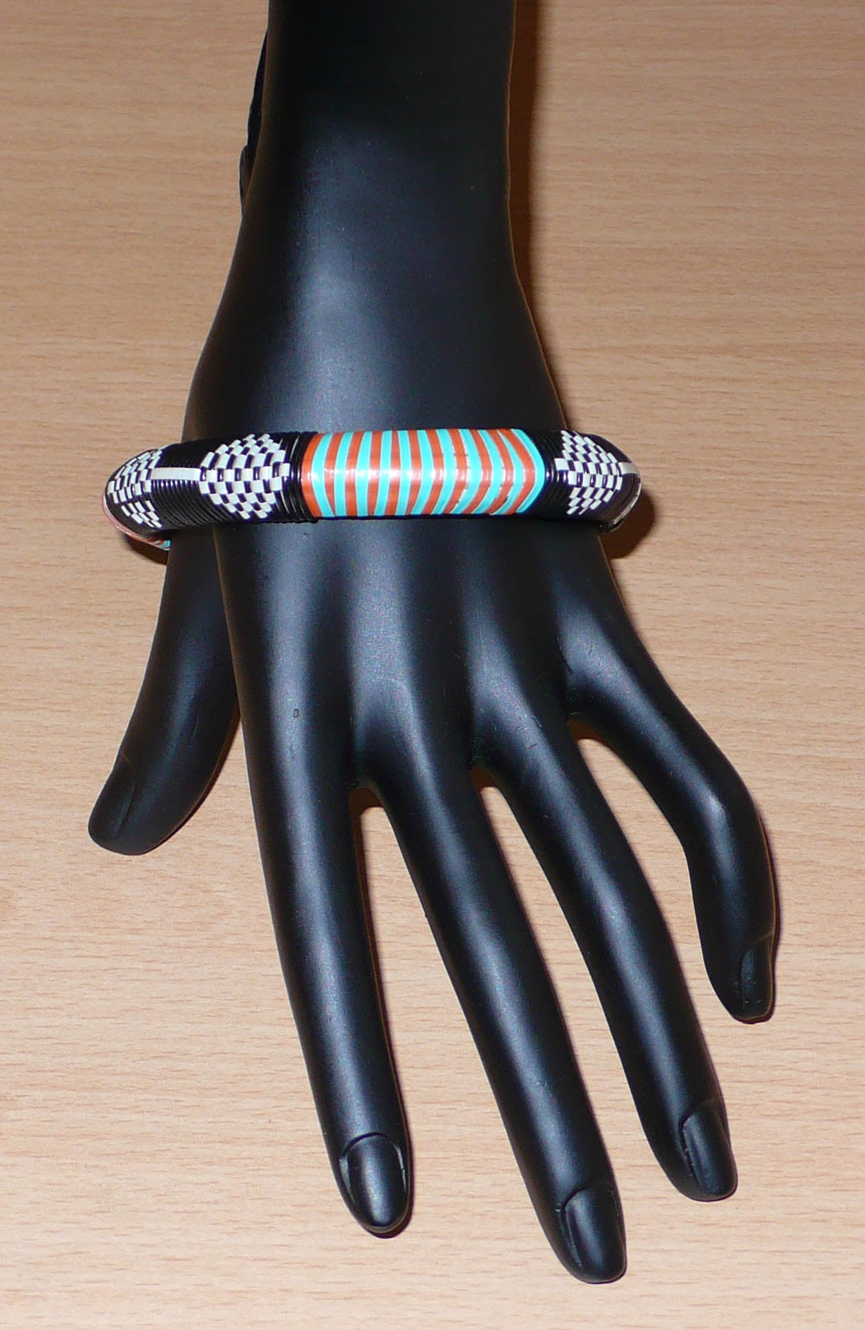 Bracelet africain à motifs tribaux, fabriqué au Mali dans une démarche eco-responsable, il est tressé à partir de fines bandes de plastique recyclé noir, blanc, orange et vert.