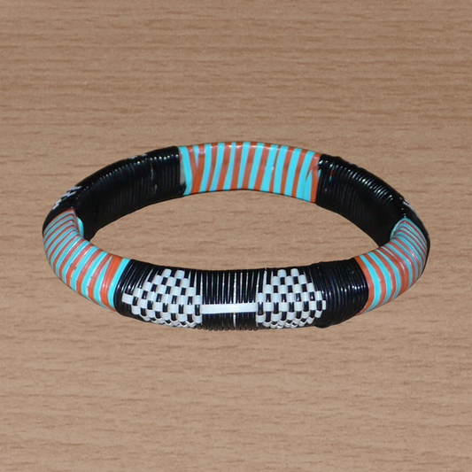 Bracelet africain à motifs tribaux, fabriqué au Mali dans une démarche eco-responsable, il est tressé à partir de fines bandes de plastique recyclé noir, blanc, orange et vert.