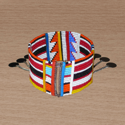 Bracelet de cheville africain traditionnel aux couleurs et motifs ethniques géométriques Massai composé de dix-huit rangées de perles de verre multicolores et décoré de chaînettes rehaussée de disques métalliques.
