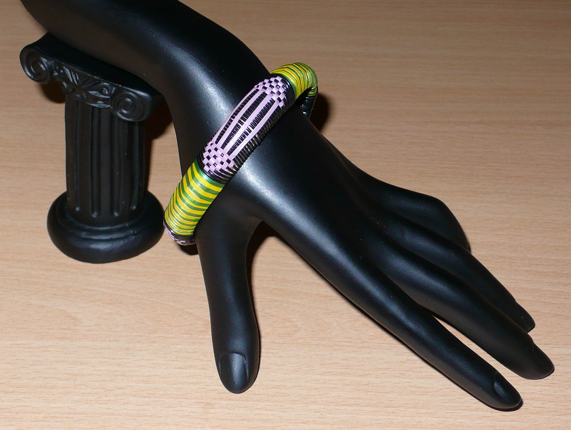 Bracelet africain écolo à motifs ethniques tissés avec des bandes de plastique recyclé noir, violet, vert et jaune.