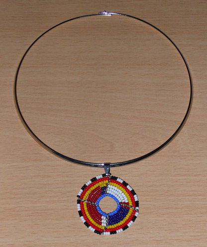 Collier africain composé d'un ras de cou en laiton orné d'un petit médaillon fait d'un tissage de perles de rocaille. Il mesure 18,5 cm de long, la circonférence du ras de cou est de 42,5 cm et son diamètre de 13,5 cm ; le médaillon mesure 4,5 cm de long et de large.