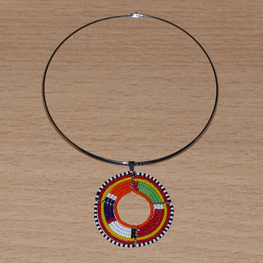 Alliance de tradition kenyane et de modernité, ce collier se compose d'un ras de cou en laiton agrémenté d'un médaillon perlé aux couleurs et motifs ethniques traditionnels Massai fait d'un tissage de perles de rocaille multicolores.