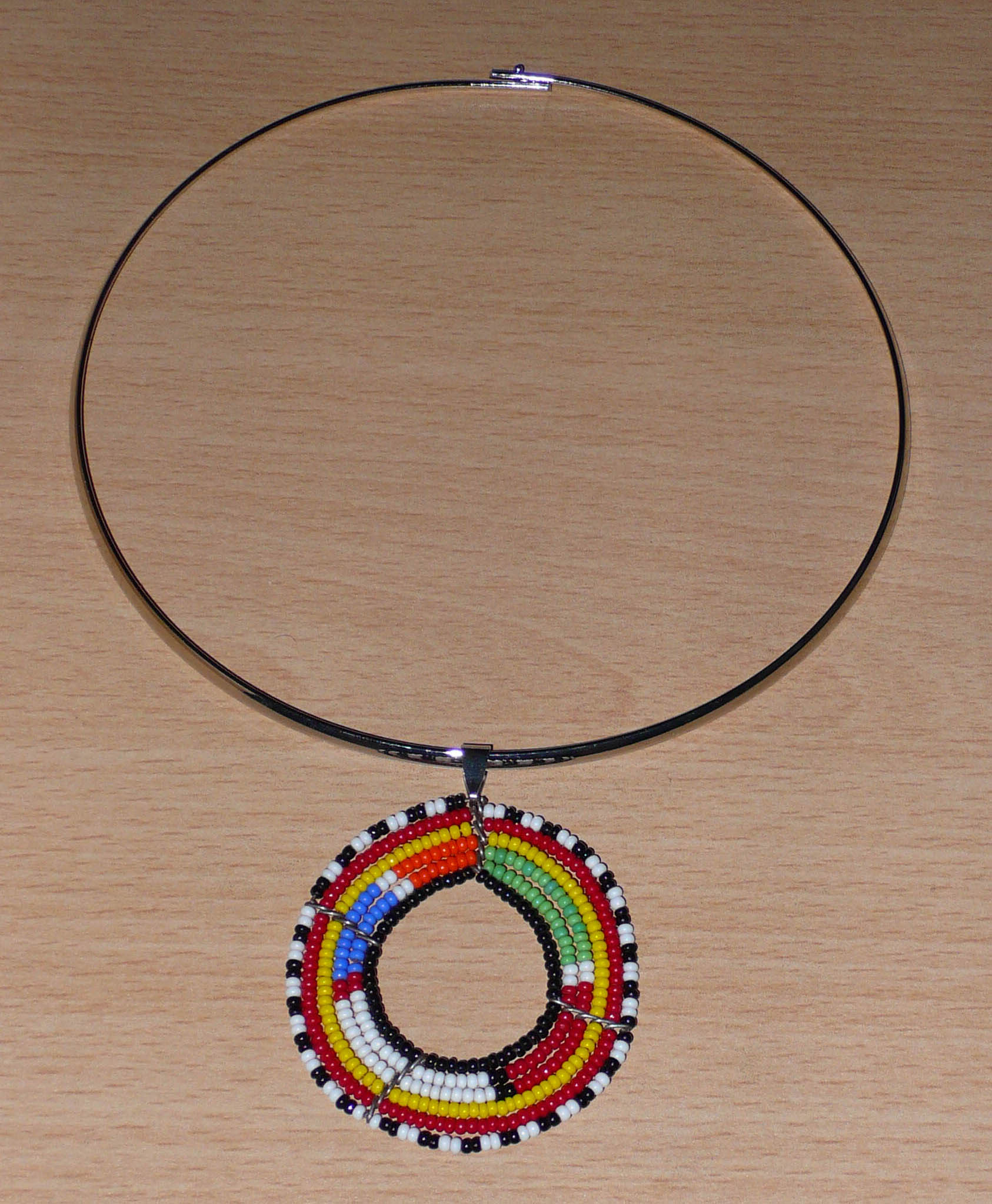 Collier africain alliant tradition kenyane et modernité se composant d'un ras de cou en laiton orné d'un médaillon perlé aux couleurs ethniques et motifs traditionnels Massai fait de perles de rocaille multicolores.