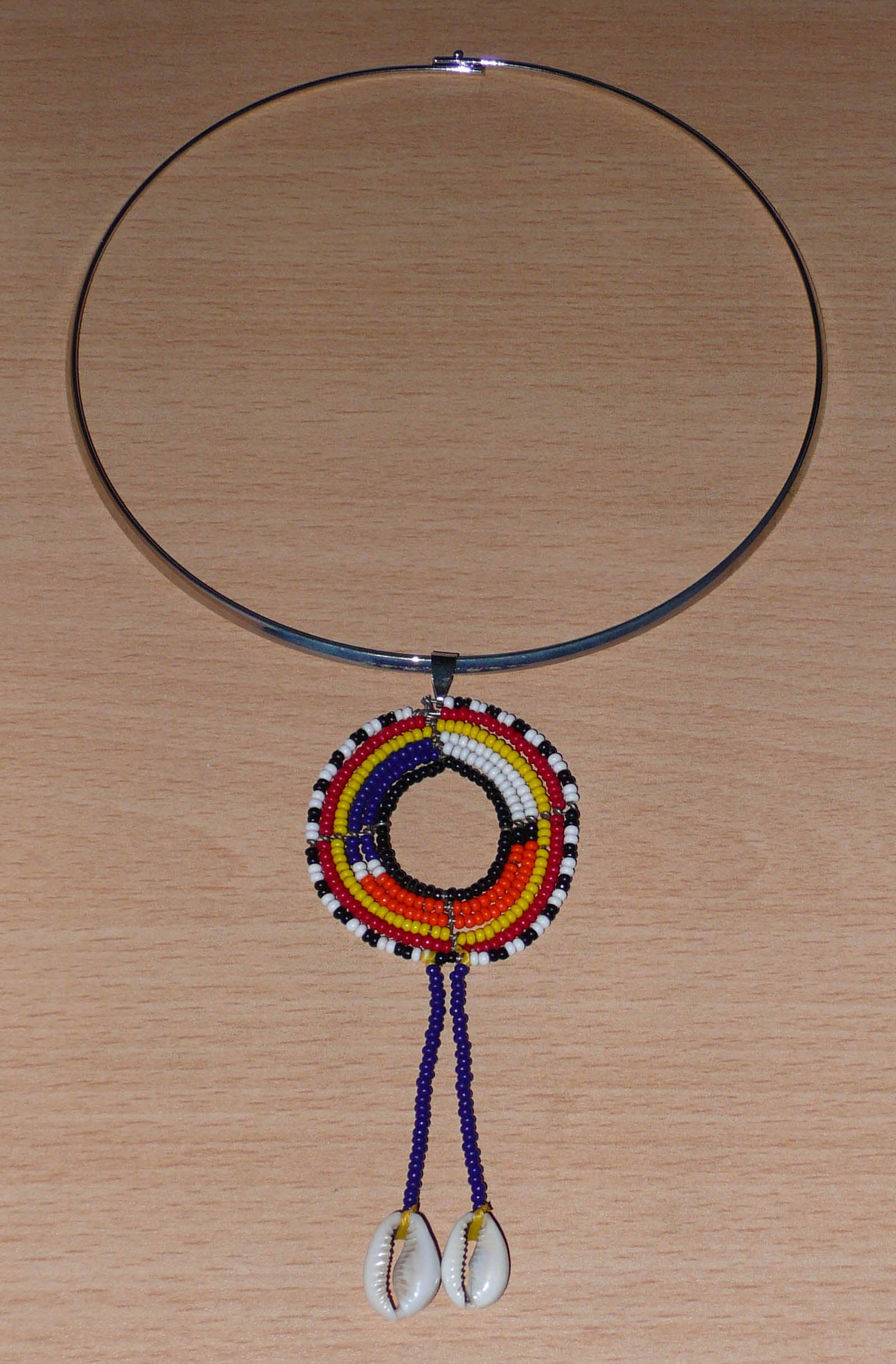Collier africain Massai composé d'un ras de cou en laiton agrémenté d'un long pendentif ethnique fait de perles de rocaille et de coquillages cauris.