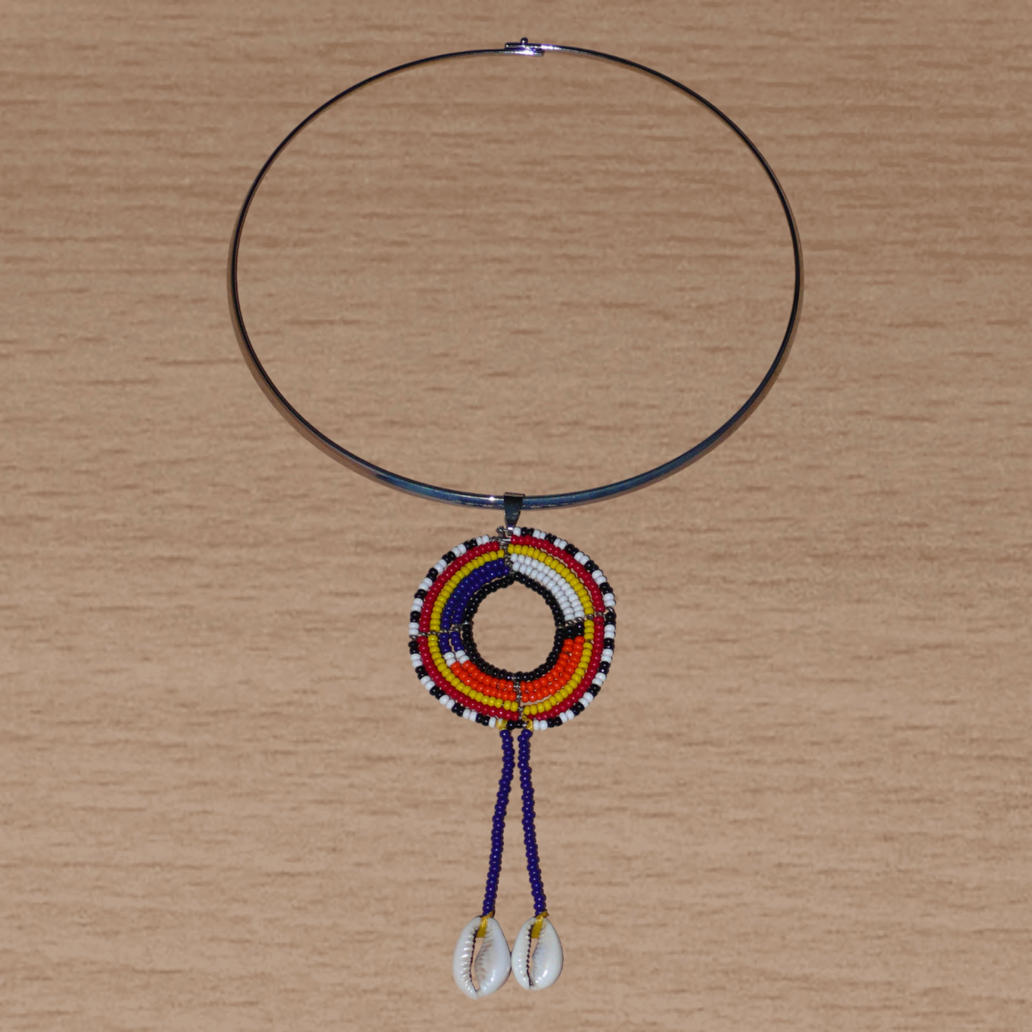 Collier africain Massai composé d'un ras de cou en laiton agrémenté d'un long pendentif ethnique fait de perles de rocaille et de coquillages cauris.