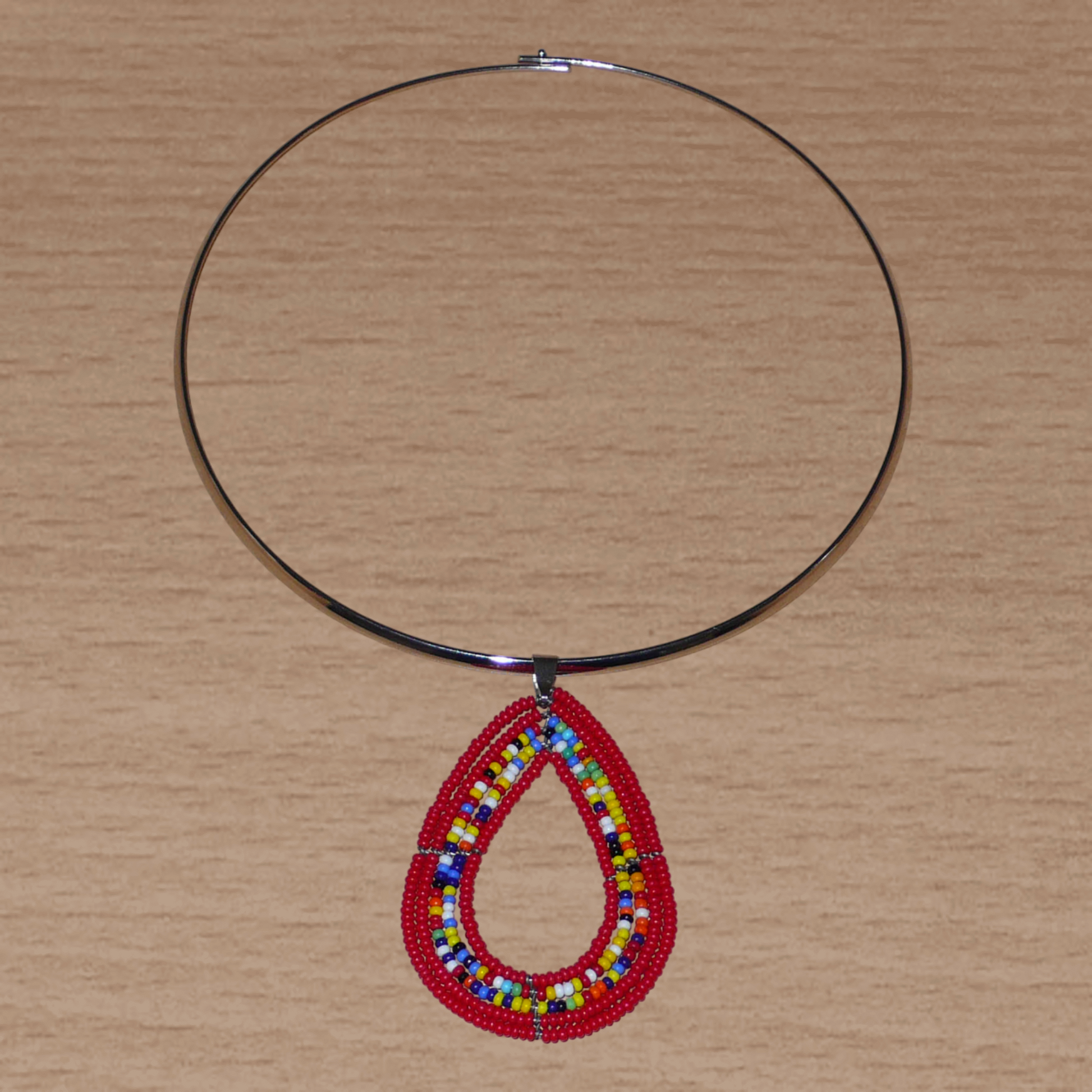 Collier ethnique de style afro bohème composé d'un ras de cou en laiton orné d'un pendentif en forme de goutte fait de perles de rocaille rouges et multicolores. Il mesure 20 cm de long, la circonférence du ras de cou en laiton est de 42,5 cm et son diamètre de 13,5 cm ; le pendentif perlé mesure 7 cm de long et 4,5 cm de large.