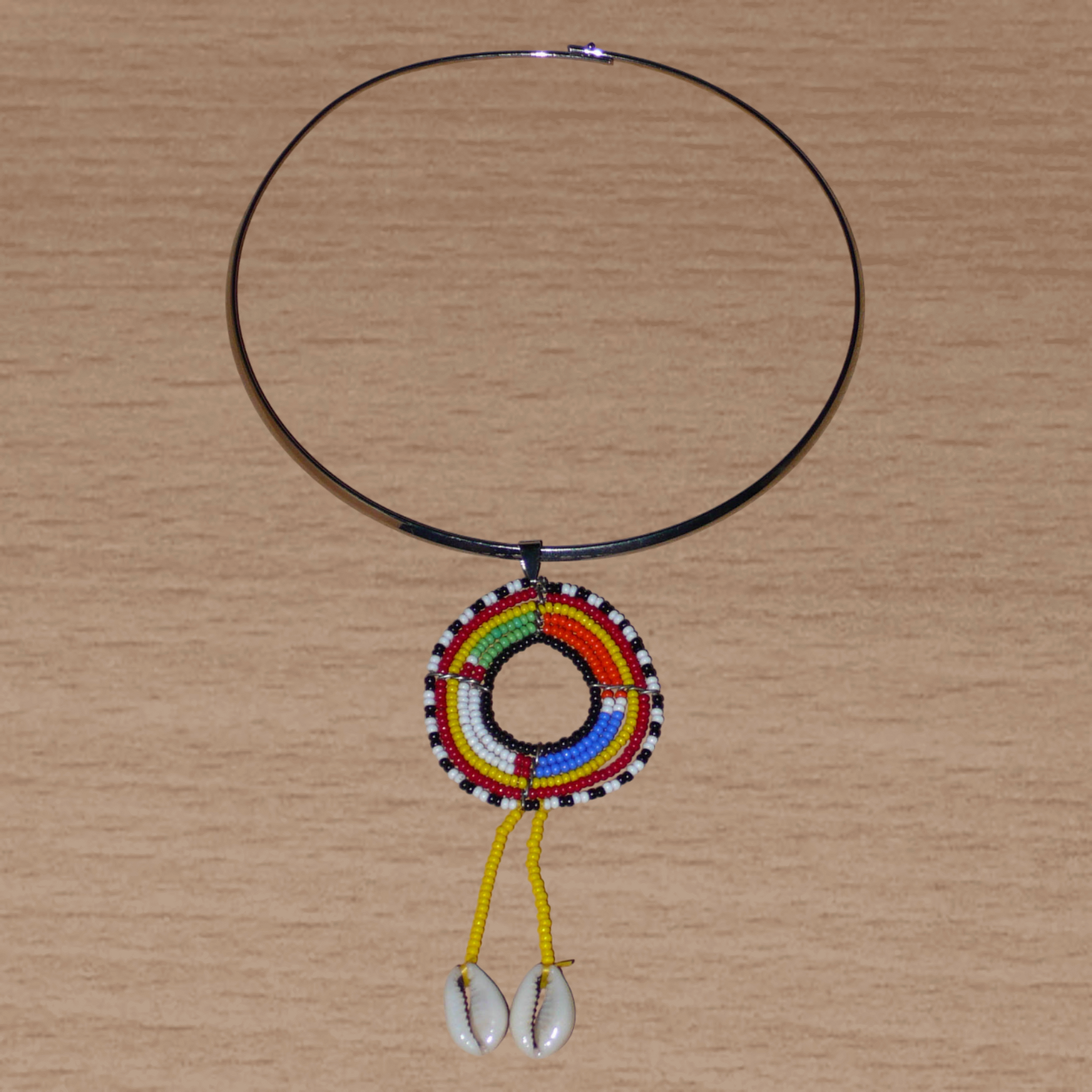 Bijou africain composé d'un collier ras de cou en laiton rehaussé d'un pendentif ethnique Massai fait de perles jaunes et multicolores et de coquillages cauris.