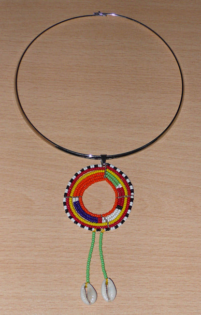 Collier africain composé d'un tour de cou en laiton orné d'un long pendentif Massai en perles de rocailles vertes et multicolores et coquillages. Timeless Fineries