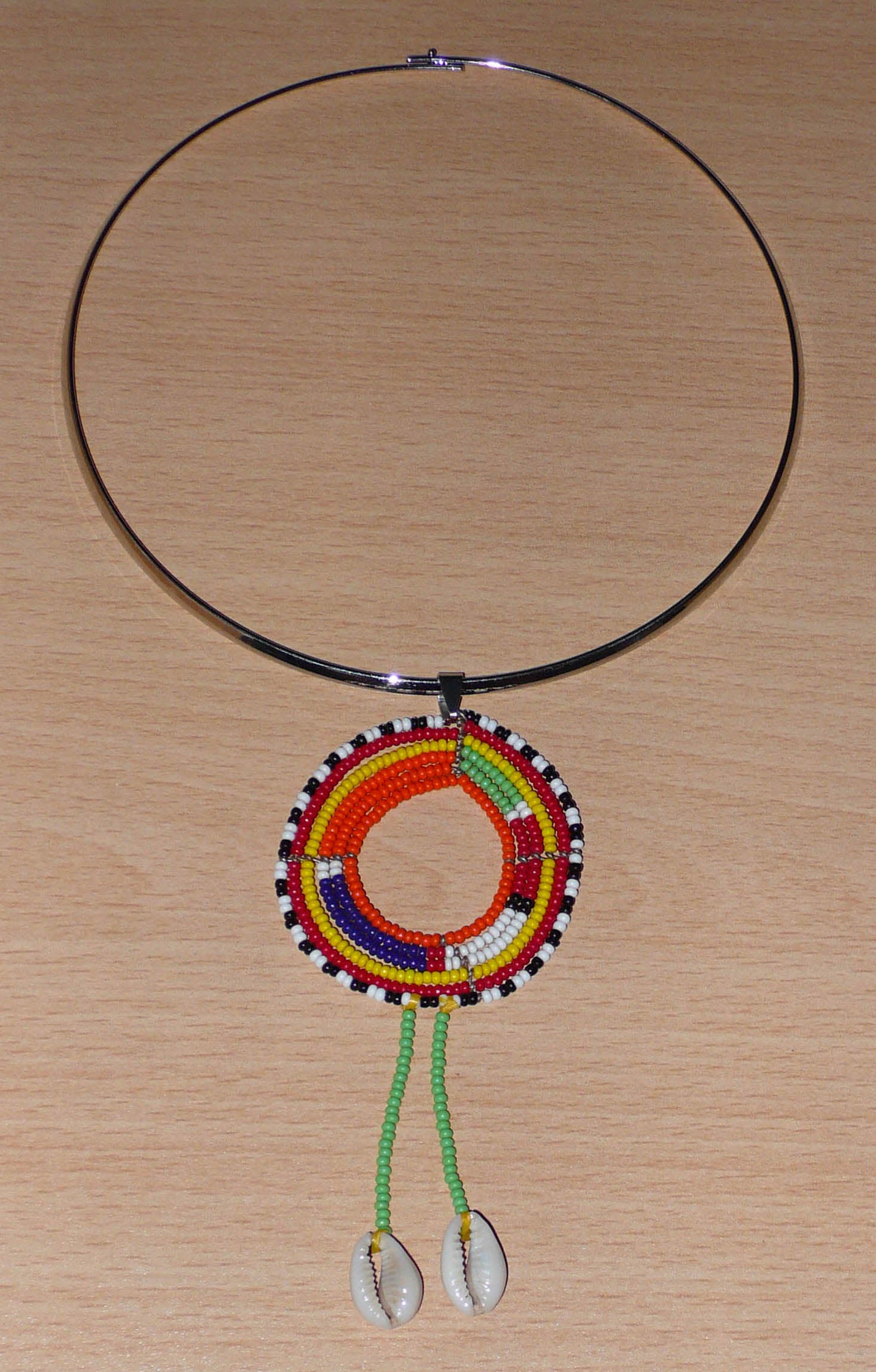 Collier africain se composant d'un ras de cou en laiton orné d'un long pendentif ethnique Massai en perles de rocaille vertes et multicolores et coquillages cauris.