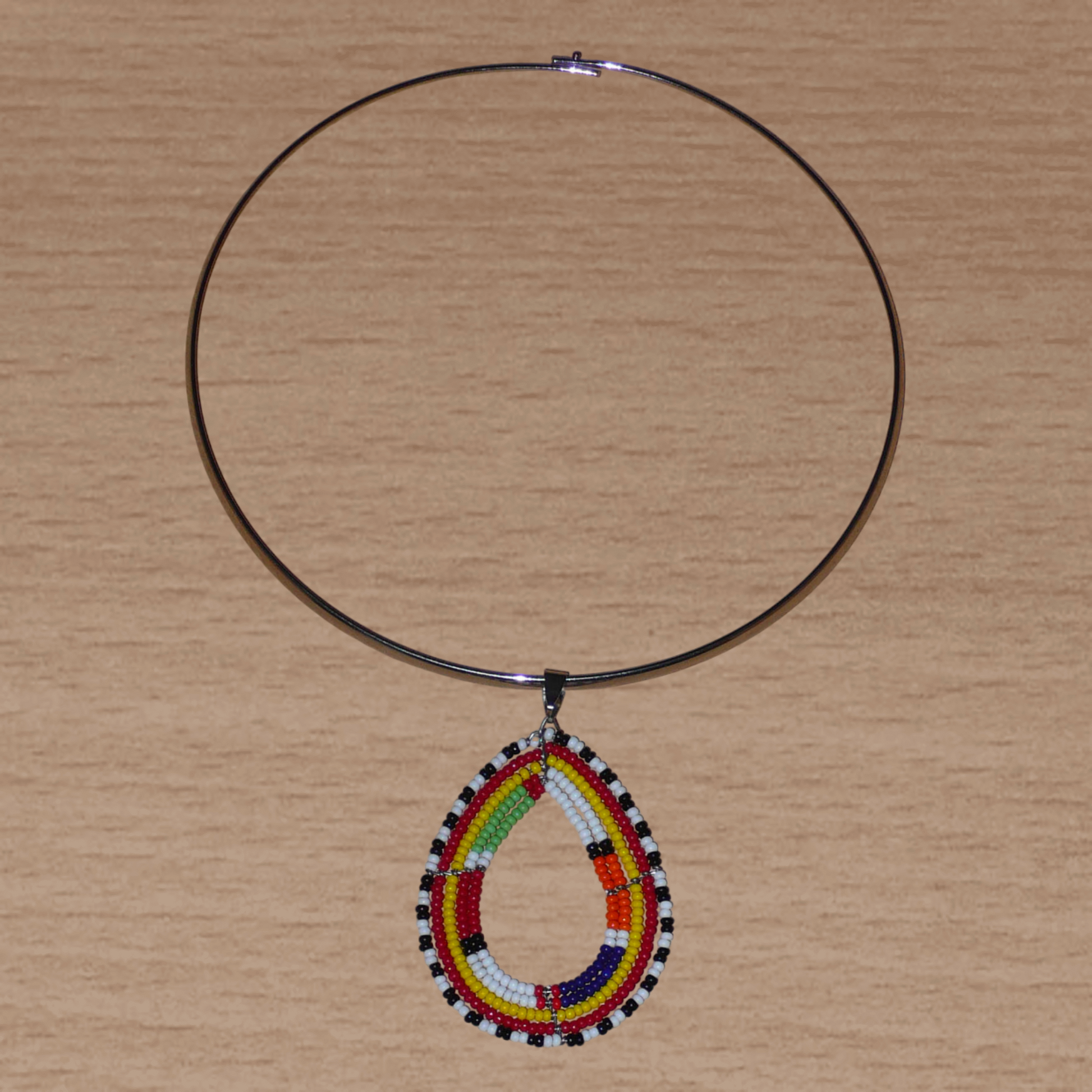 Alliance de tradition Massai et de modernité, ce collier ethnique chic se compose d'un ras de cou en laiton orné d'un pendentif en forme de goutte fait de perles de rocaille multicolores.