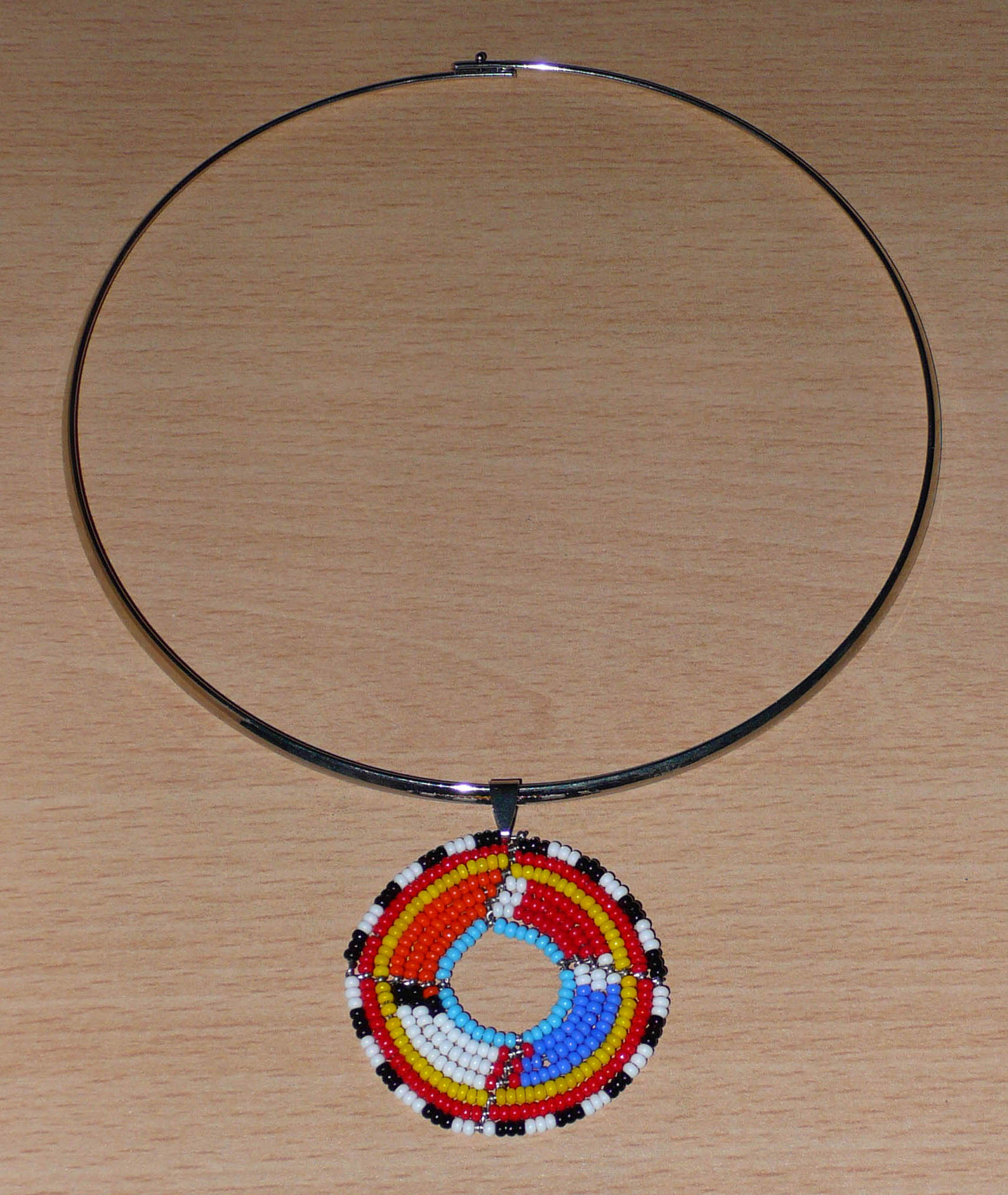 Bijou africain ethnique composé d'un collier ras de cou en laiton orné d'un petit médaillon Massai fait de perles de rocaille multicolores.
