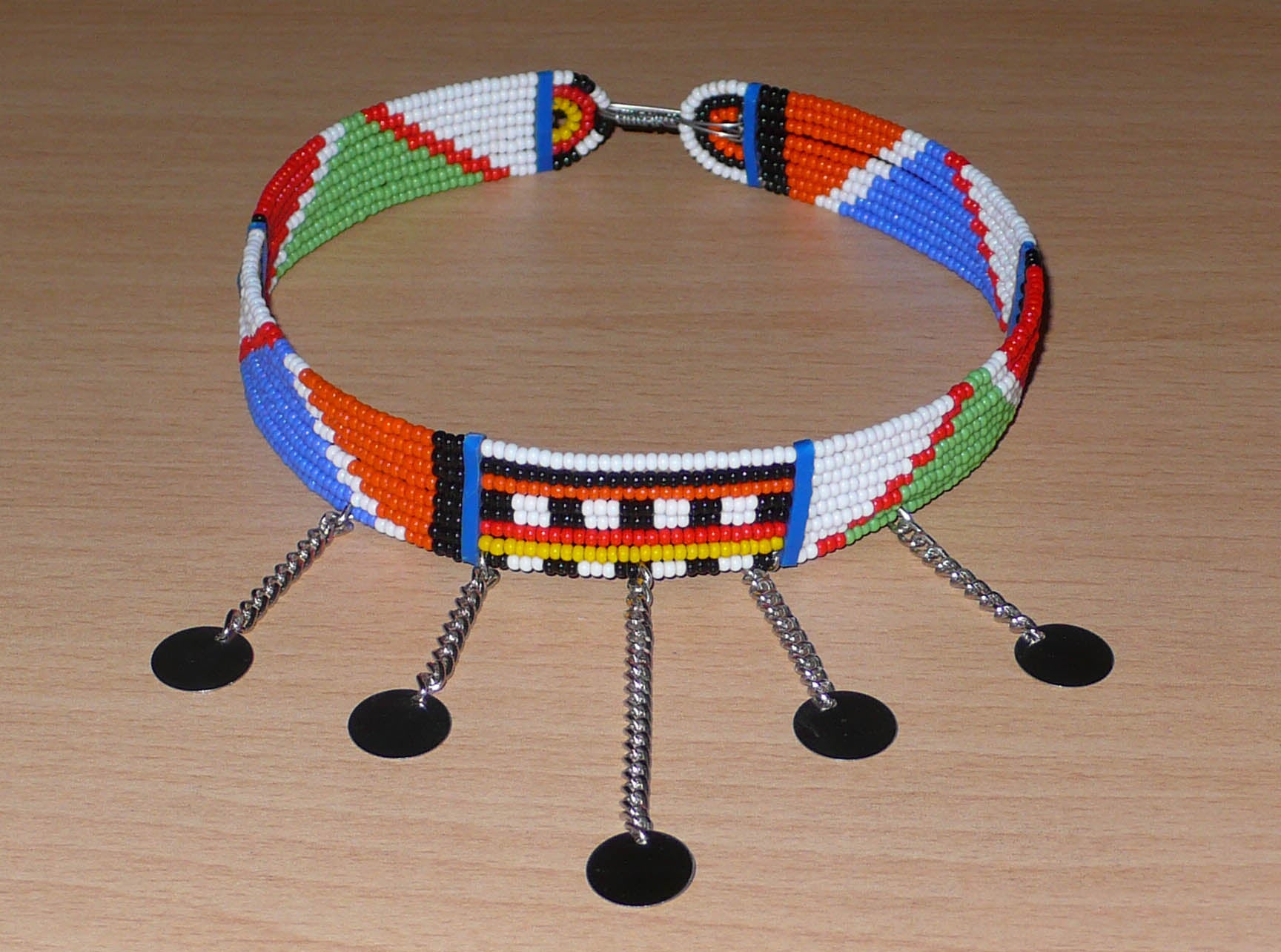 Collier africain Massai à motifs ethniques traditionnels composé de huit rangées de perles de rocaille multicolores et décoré de chaînettes ornées de disques métalliques.