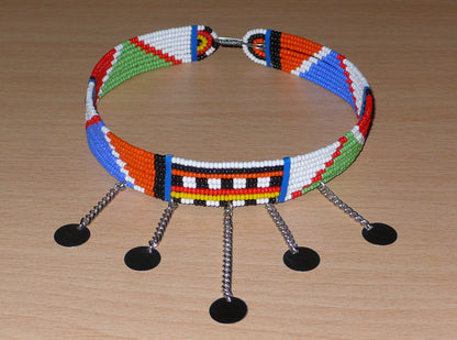 Collier africain Massai à motifs ethniques traditionnels composé de huit rangées de perles de rocaille multicolores et décoré de chaînettes ornées de disques métalliques.