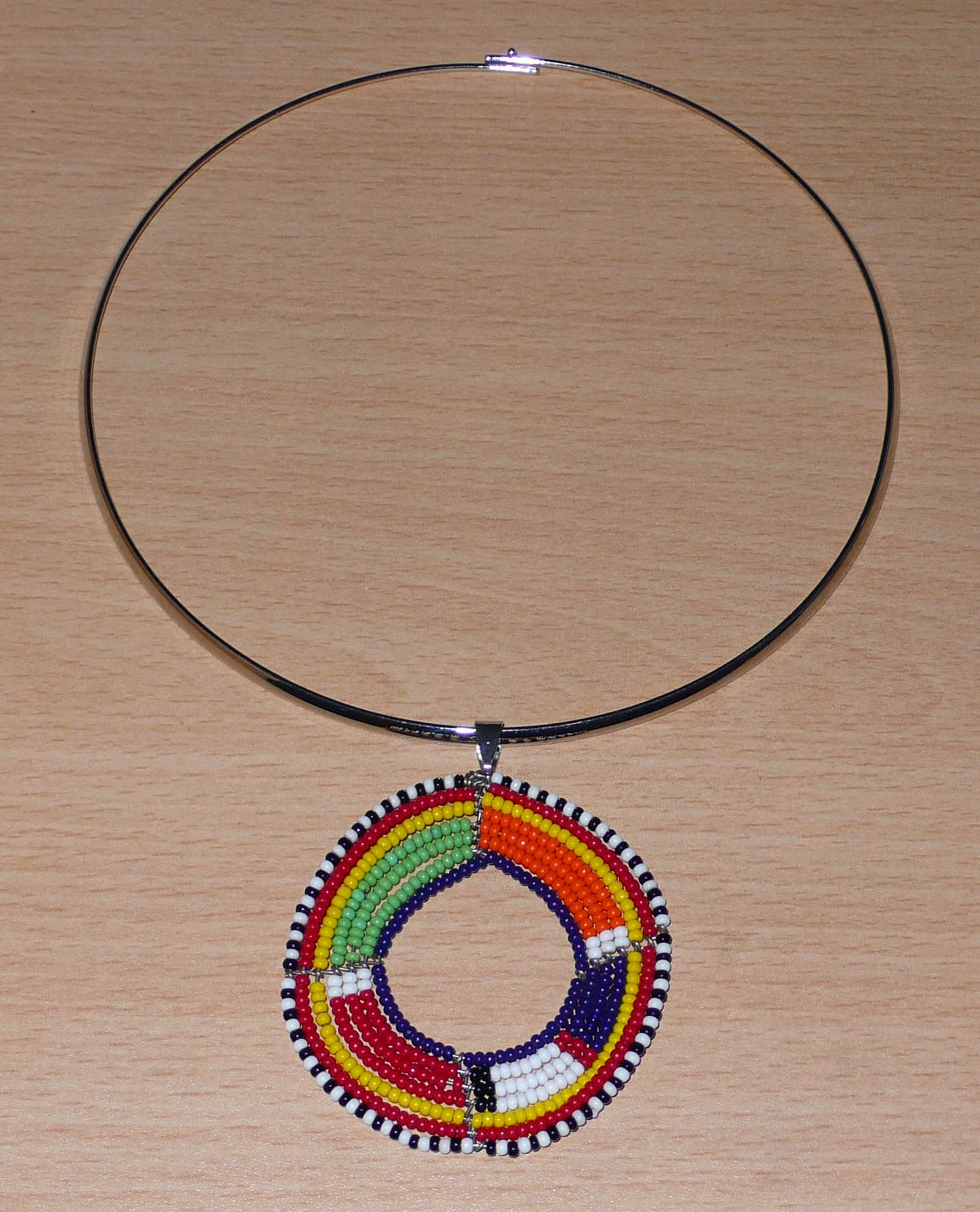 Bijou africain composé d'un collier ras de cou en laiton rehaussé d'un pendentif Massai rond fait de perles de rocaille multicolores.