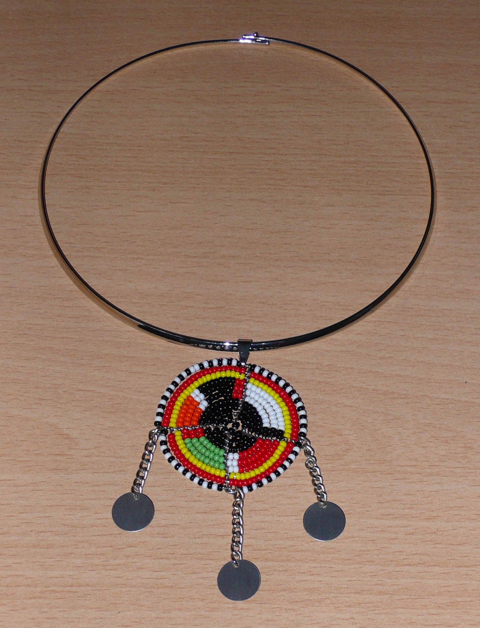 Bijou africain composé d'un ras de cou en laiton agrémenté d'un pendentif fait de perles de rocaille noires et multicolores et décoré de petits disques métalliques. 