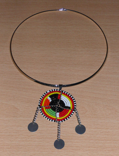 Bijou africain composé d'un ras de cou en laiton agrémenté d'un pendentif fait de perles de rocaille noires et multicolores et décoré de petits disques métalliques. 