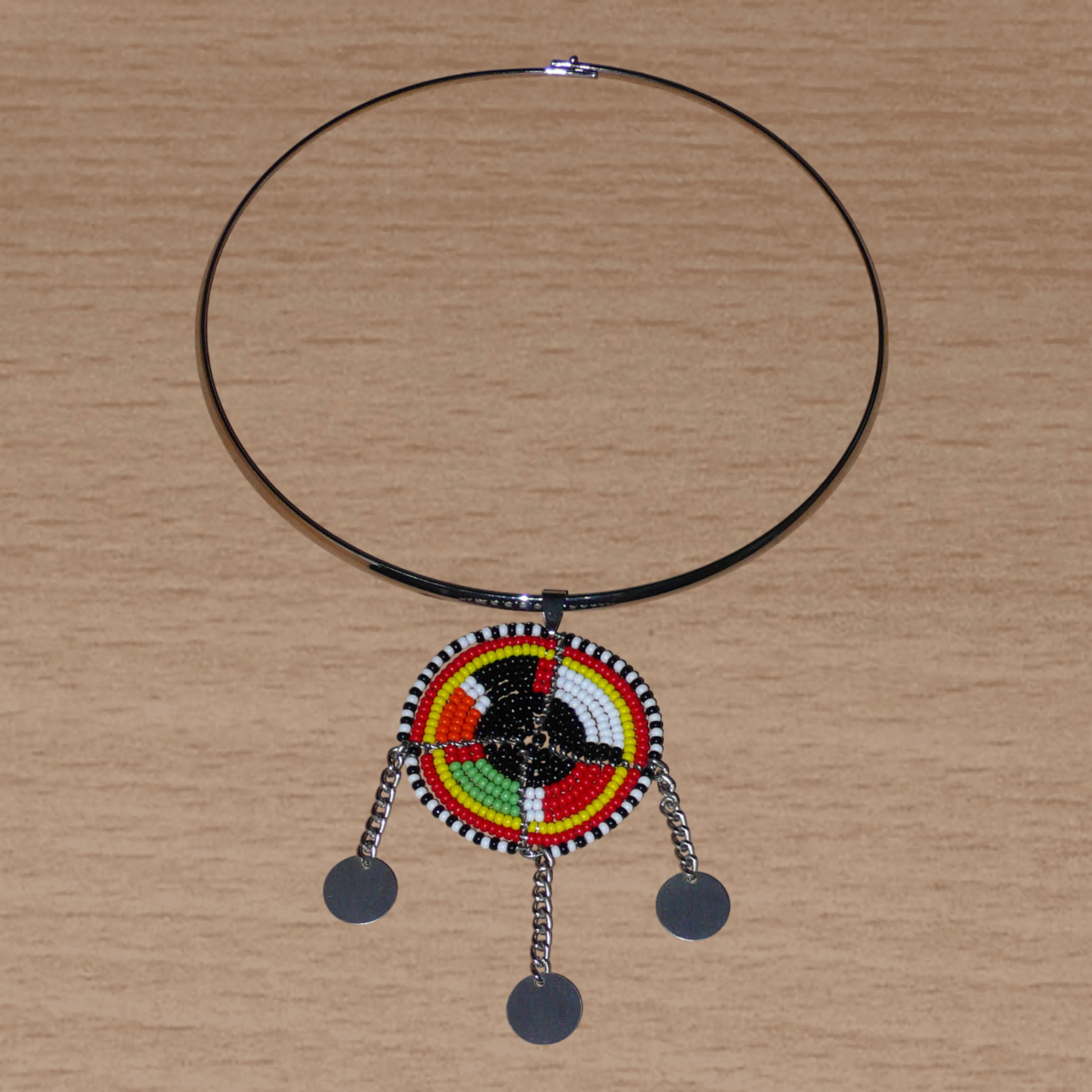 Bijou africain composé d'un ras de cou en laiton agrémenté d'un pendentif fait de perles de rocaille noires et multicolores et décoré de petits disques métalliques.