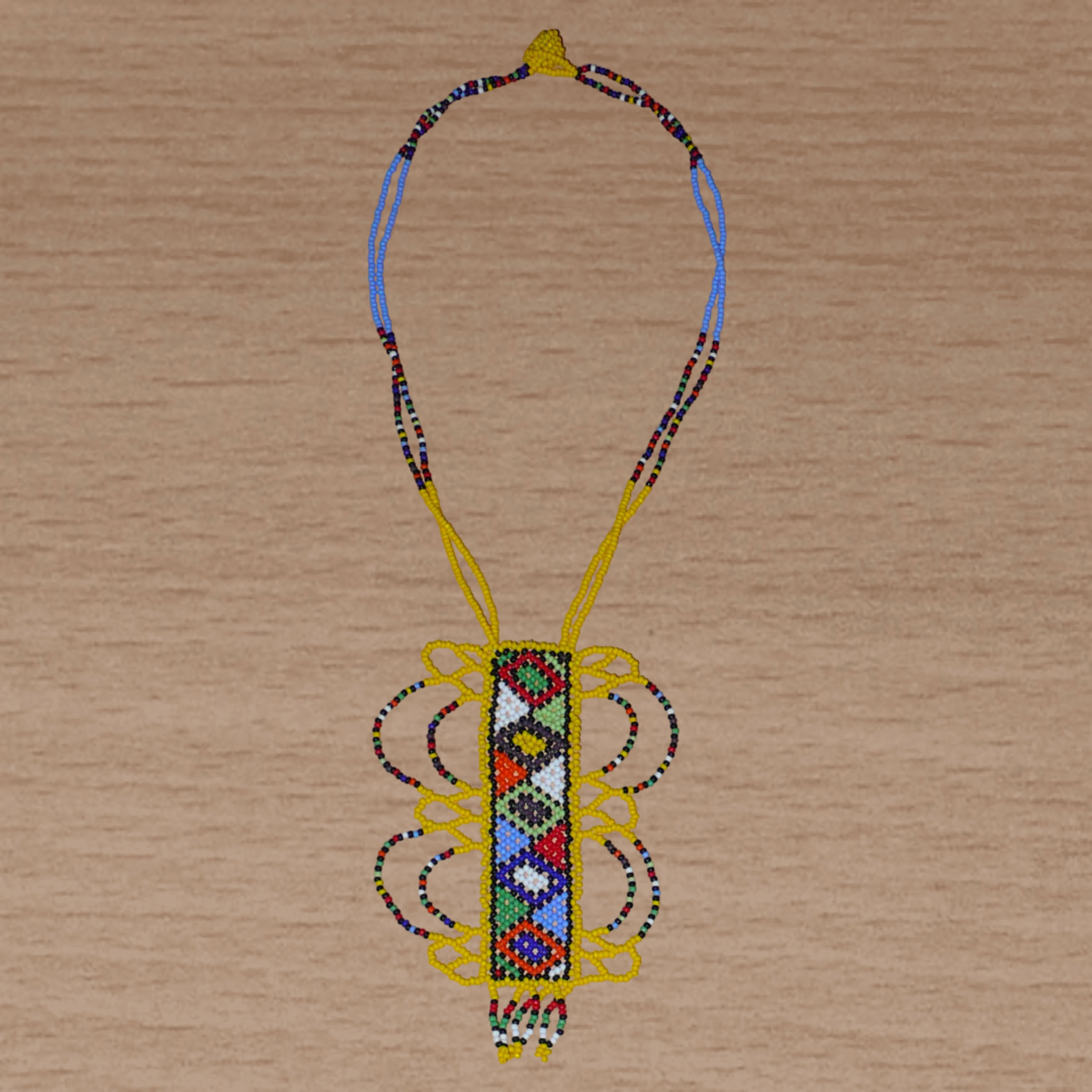 Collier sud-africain jaune orné d'un long pendentif fantaisie décoré de motifs ethniques zoulous multicolores ; il se compose de perles de rocaille et s'attache avec un fermoir à boule.