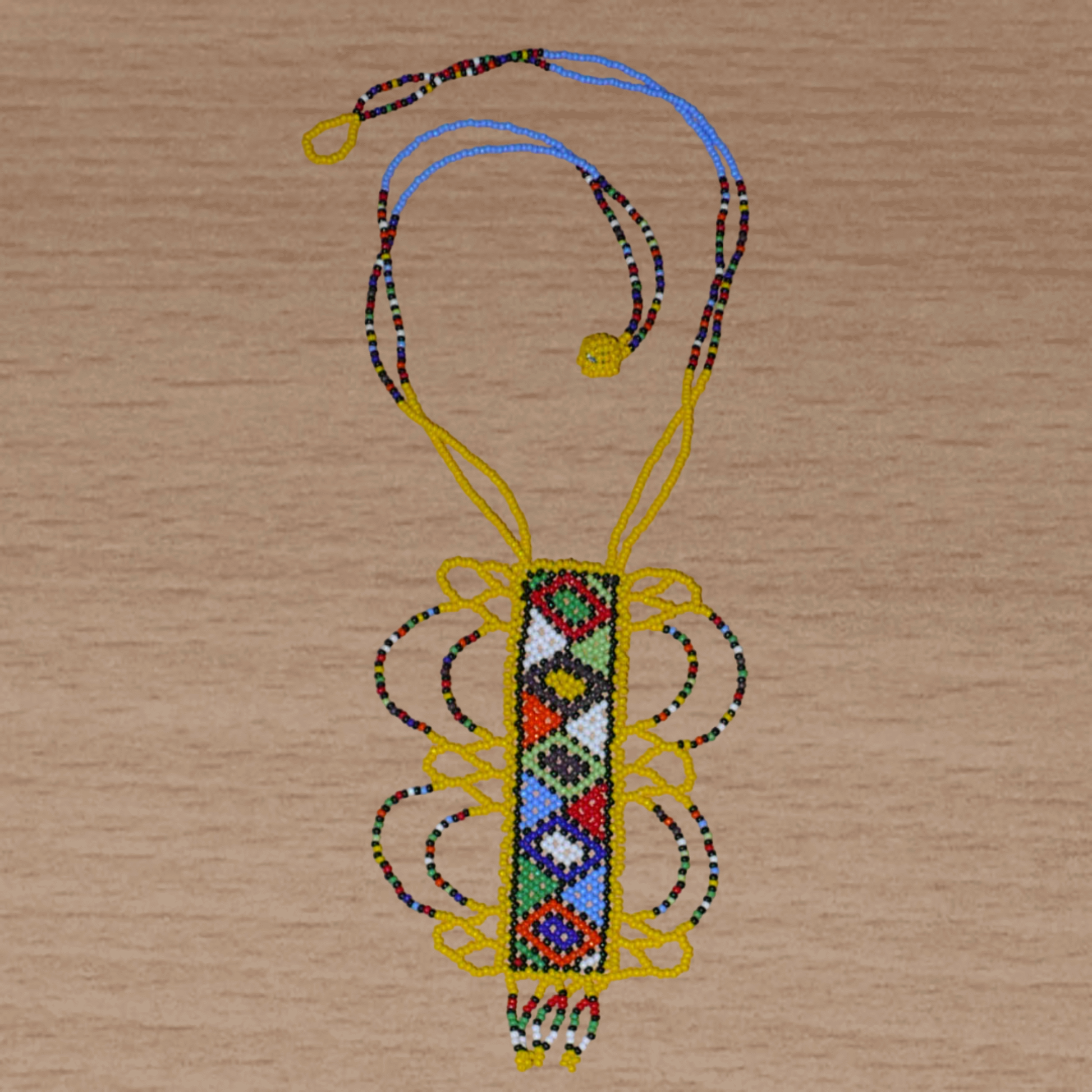 Collier sud-africain jaune orné d'un long pendentif fantaisie décoré de motifs ethniques zoulous multicolores ; il se compose de perles de rocaille et s'attache avec un fermoir à boule.