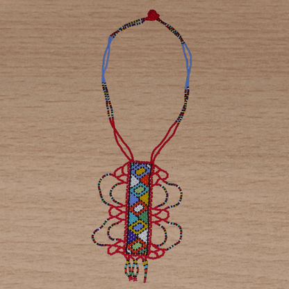 Collier sud-africain zoulou rouge et multicolore agrémenté d'un long et large pendentif fantaisie à motifs ethniques traditionnels. Il se compose de perles de rocaille et s'attache avec un fermoir à boule.