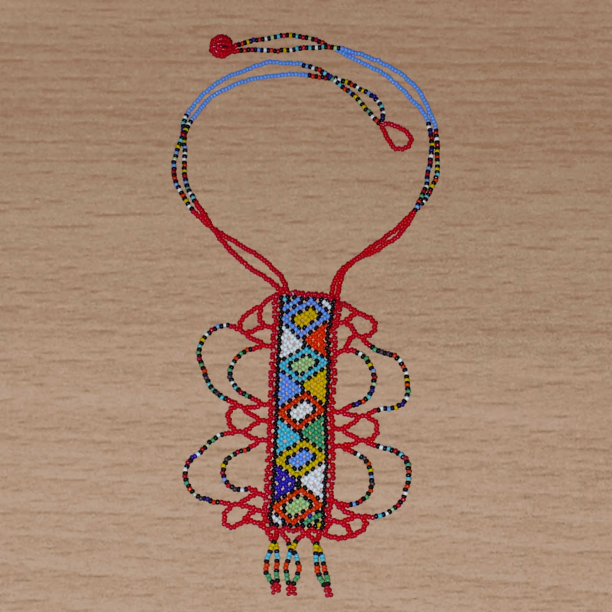 Collier sud-africain zoulou rouge et multicolore agrémenté d'un long et large pendentif fantaisie à motifs ethniques traditionnels. Il se compose de perles de rocaille et s'attache avec un fermoir à boule.
