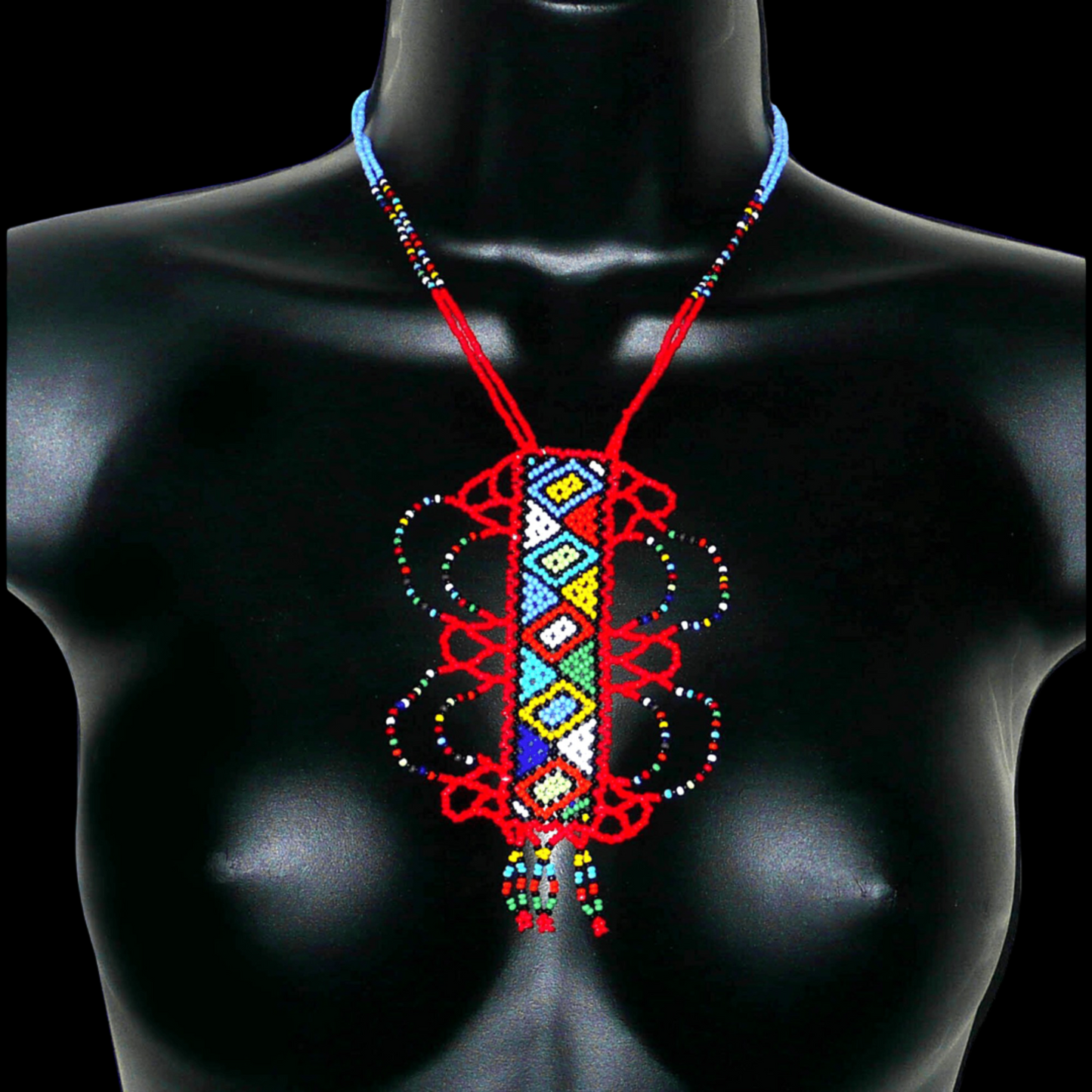 Collier sud-africain zoulou rouge et multicolore agrémenté d'un long et large pendentif fantaisie à motifs ethniques traditionnels. Il se compose de perles de rocaille et s'attache avec un fermoir à boule.