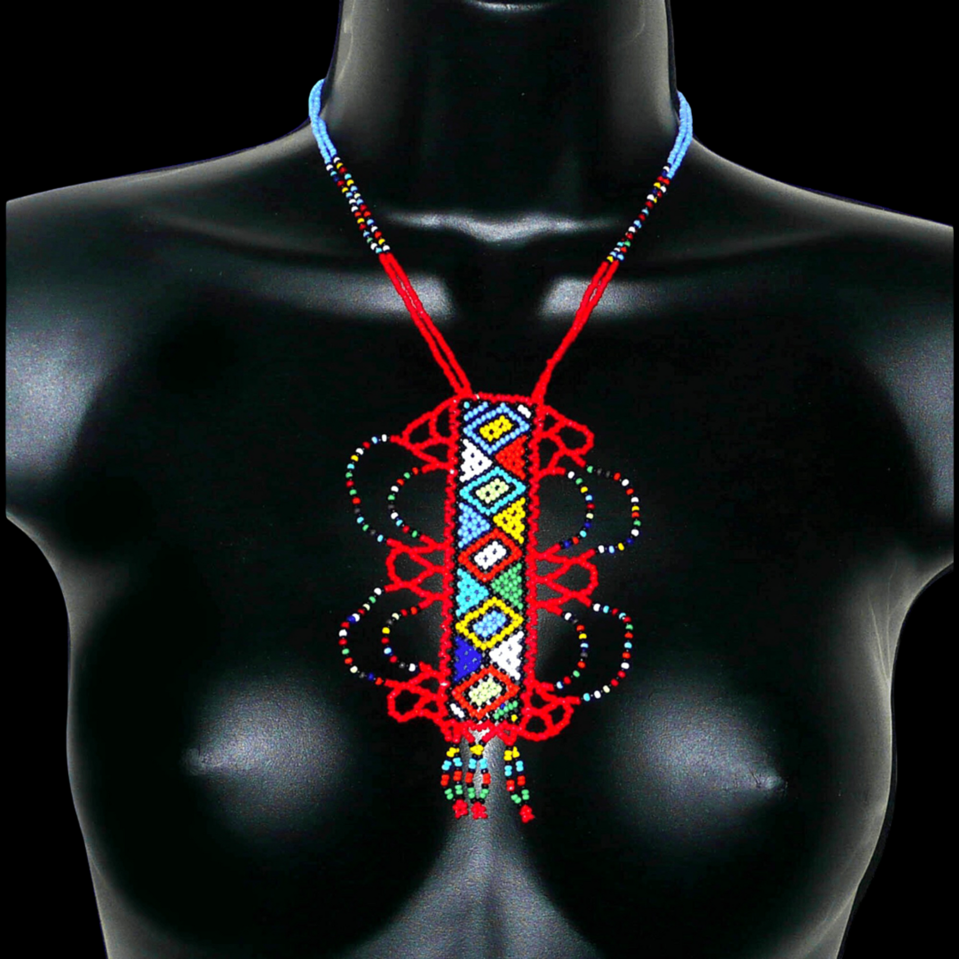 Collier sud-africain zoulou rouge et multicolore agrémenté d'un long et large pendentif fantaisie à motifs ethniques traditionnels. Il se compose de perles de rocaille et s'attache avec un fermoir à boule.