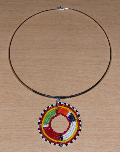 Collier africain composé d'un ras de cou en laiton rehaussé d'un médaillon Massai fait de perles de rocaille rouges et multicolores.