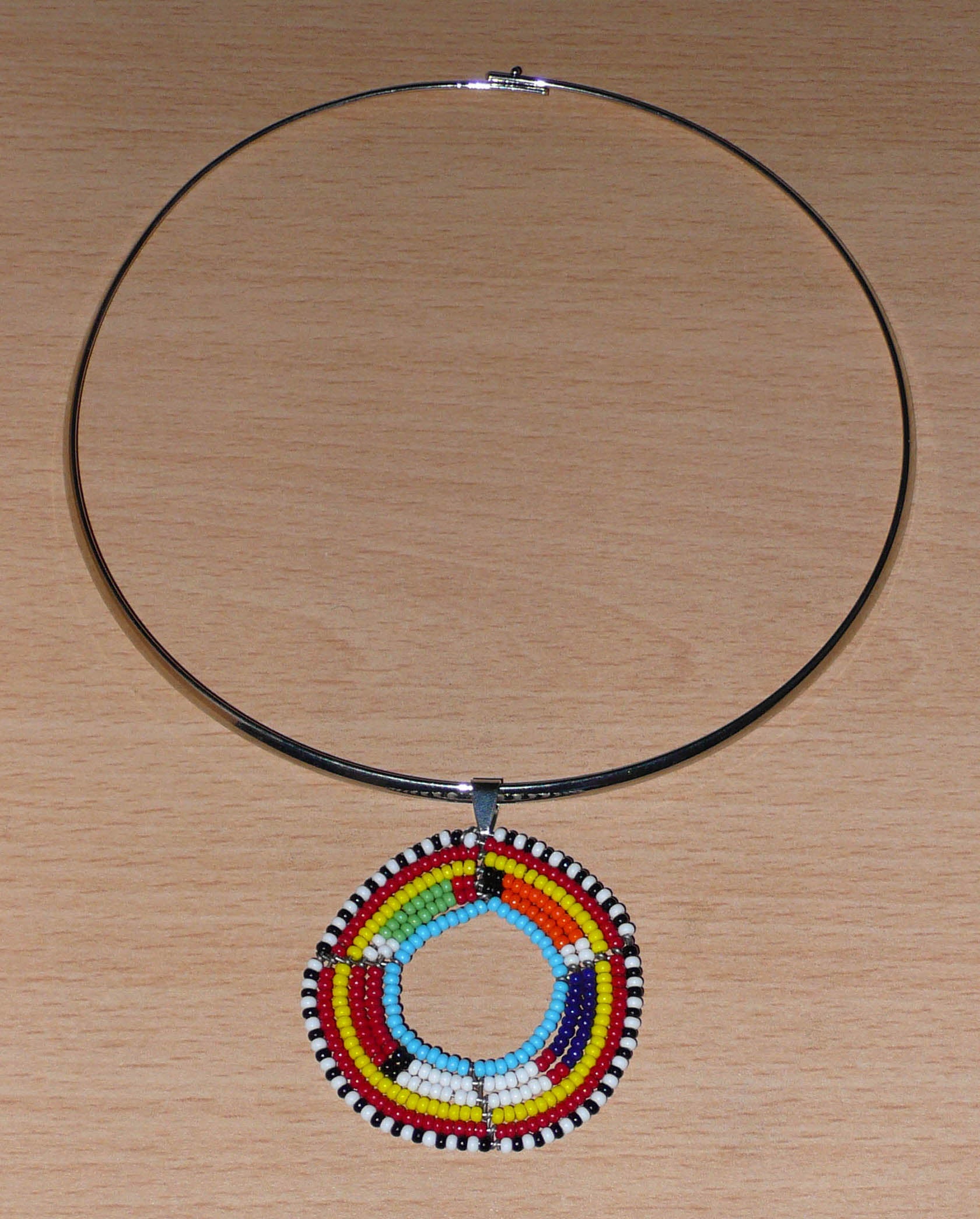 Collier africain ethnique composé d'un ras de cou en laiton agrémenté d'un médaillon traditionnel Massai fait de perles de rocaille multicolores.