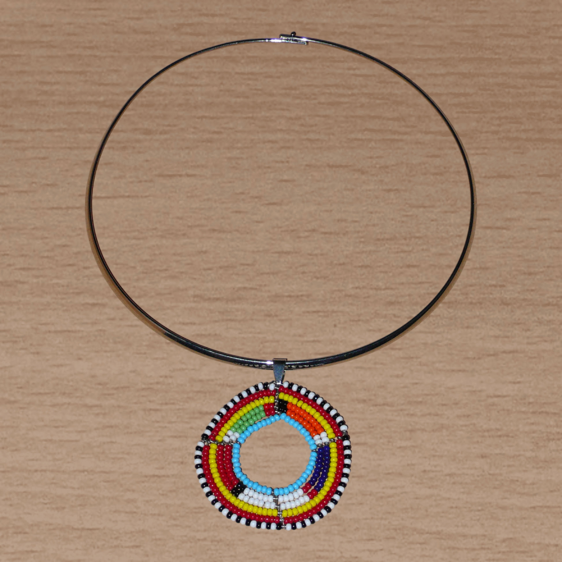 Collier africain ethnique composé d'un ras de cou en laiton agrémenté d'un médaillon traditionnel Massai fait de perles de rocaille multicolores.
