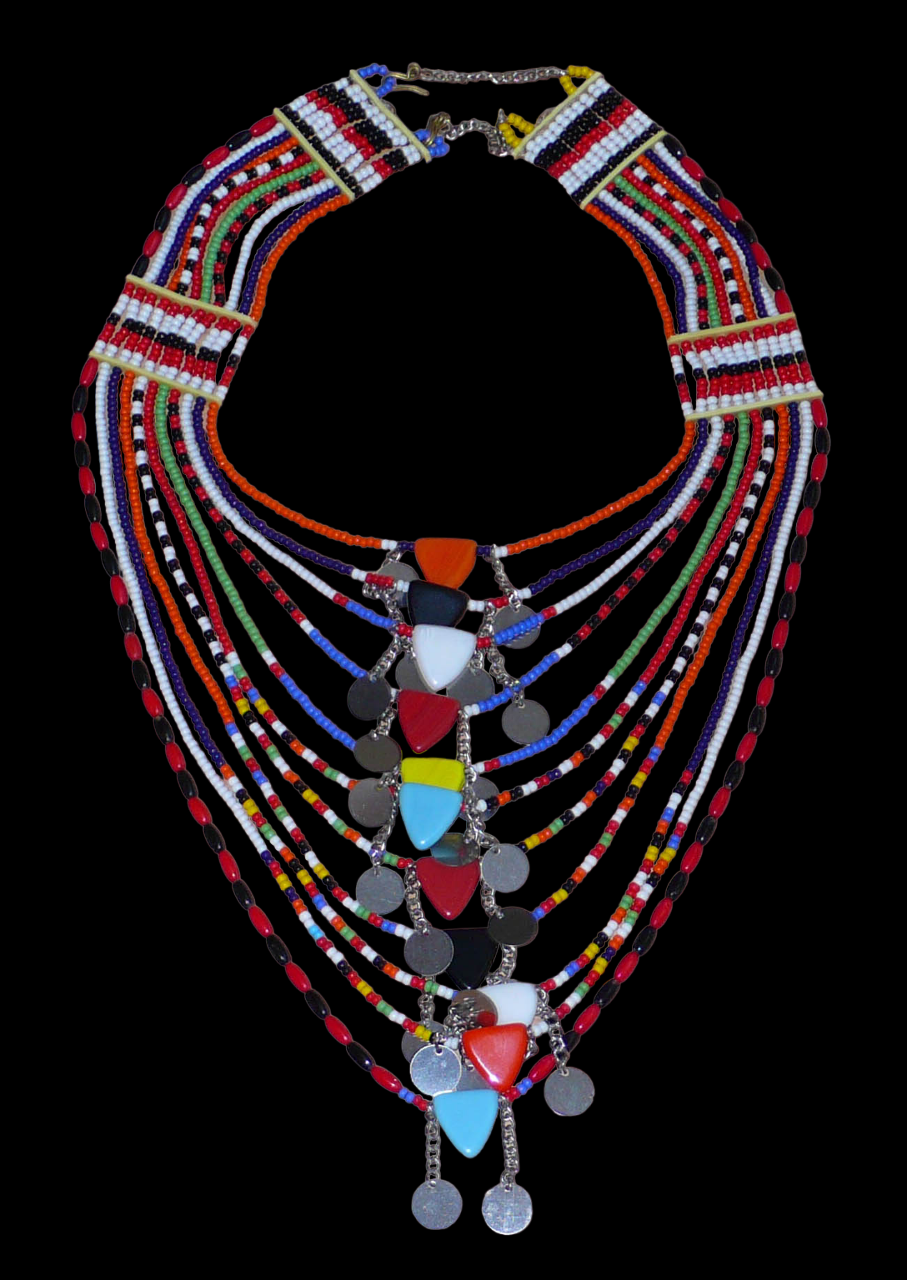Collier africain traditionnel Massai composé de onze rangées de perles de rocaille et de plastique multicolores. Des perles triangulaires colorées et des pastilles en métal décorent le collier en son centre. Il mesure 38 cm de long, avec une longueur de tour de cou de 46 cm. Il est ici présenté sur un fond noir. Timeless Fineries