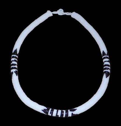 Collier sud-africain tubulaire blanc et noir. Il se compose d'un tube de plastique autour duquel sont enroulées des perles de rocaille blanches en alternance avec des motifs ethniques zoulous noirs. Le collier mesure 19 cm de long (de la nuque jusqu'à la base du collier), la longueur du tour de cou du collier est 49 cm, et son épaisseur est de 1 cm. Il s'attache avec un fermoir à boule.