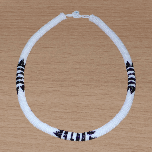 Collier africain zoulou blanc à motifs ethniques traditionnels noirs composé perles de rocaille tissées et enroulées autour d'un tube.