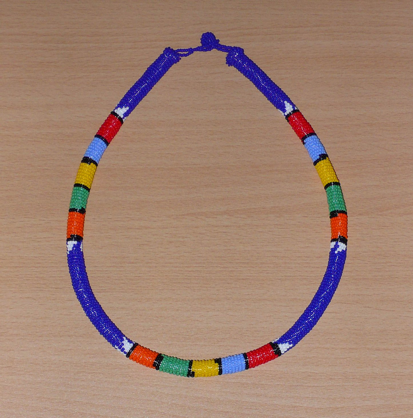 Collier sud-africain tubulaire bleu à motifs zoulous multicolores composé de perles de rocaille enroulées autour d'un tube.