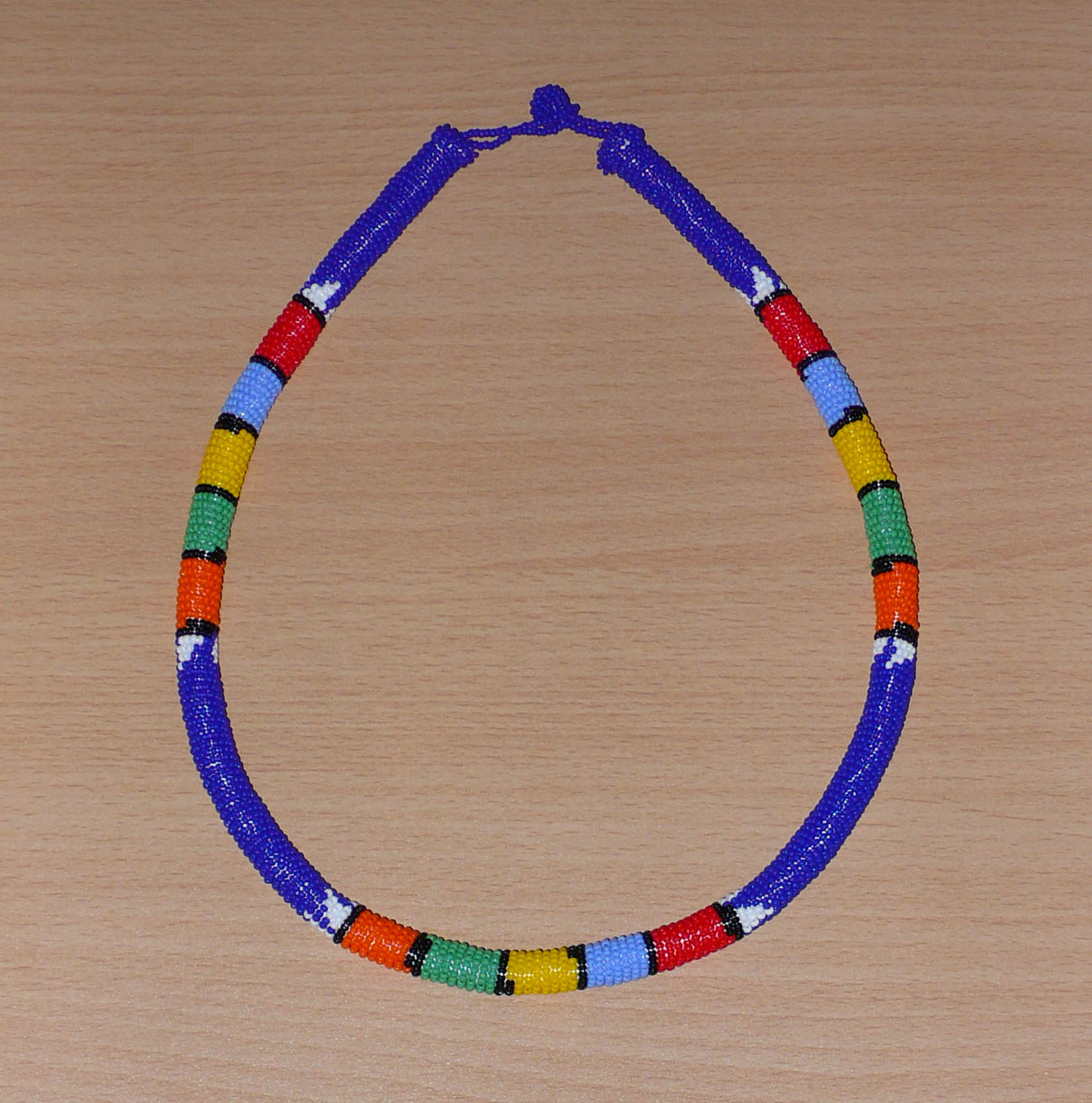 Collier sud-africain tubulaire bleu à motifs zoulous multicolores composé de perles de rocaille enroulées autour d'un tube.