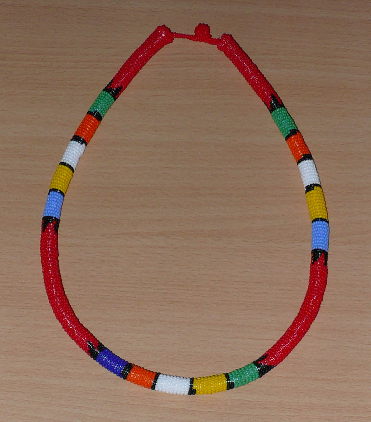 Collier africain traditionnel rouge à motifs zoulous multicolores fabriqué en Afrique du Sud ; il se compose de perles de rocaille enroulées autour d'un tube en plastique.