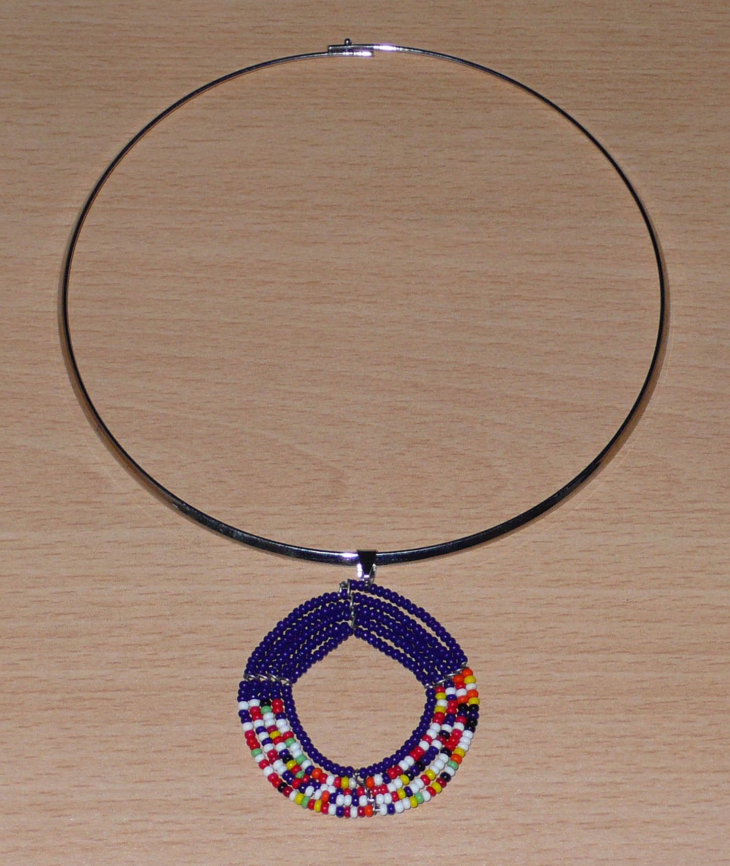 Bijou ethnique afro chic composé d'un collier ras de cou en laiton orné d'un médaillon Massai fait de perles de rocaille bleu foncé et multicolores.