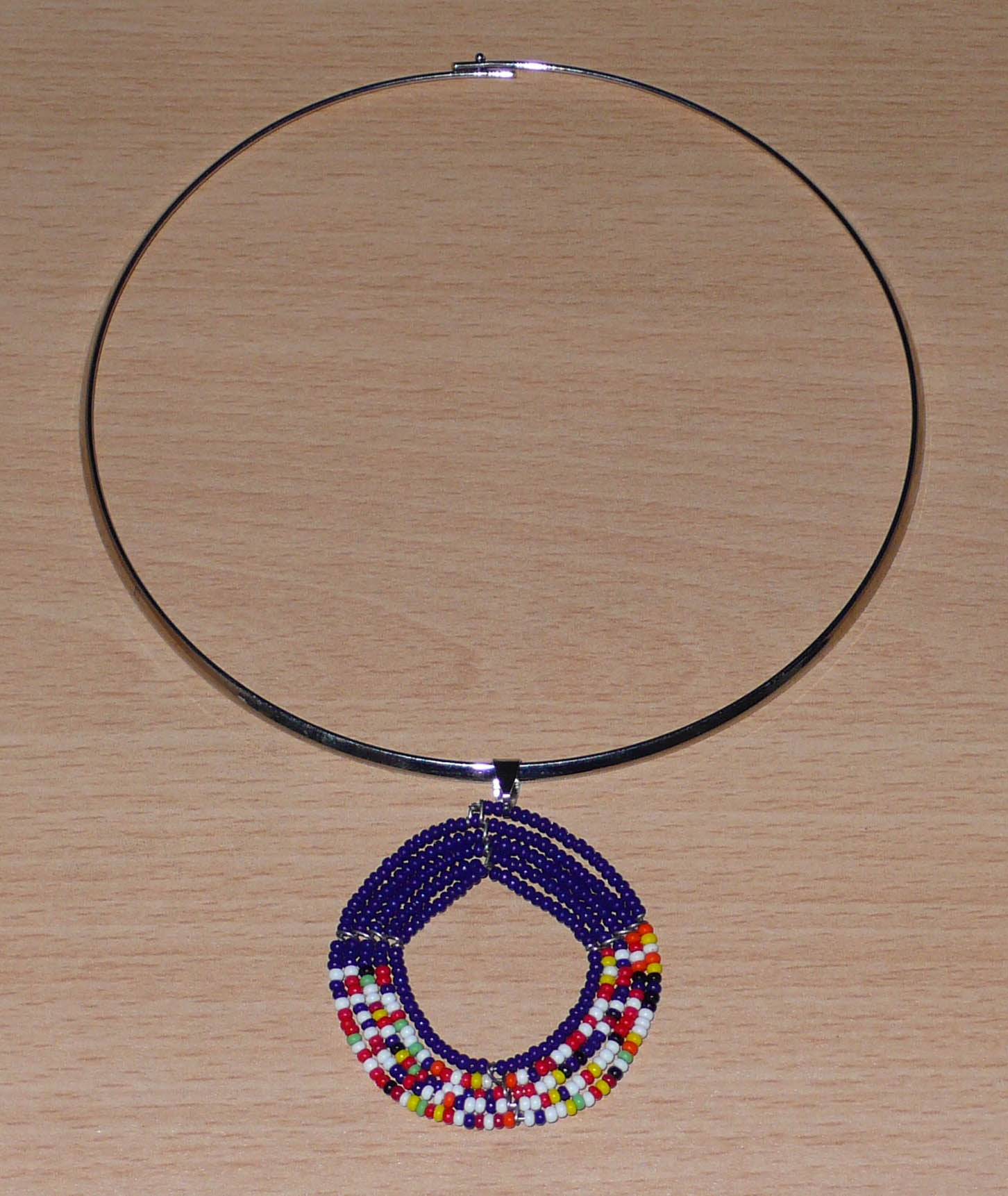 Bijou ethnique afro chic composé d'un collier ras de cou en laiton orné d'un médaillon Massai fait de perles de rocaille bleu foncé et multicolores.
