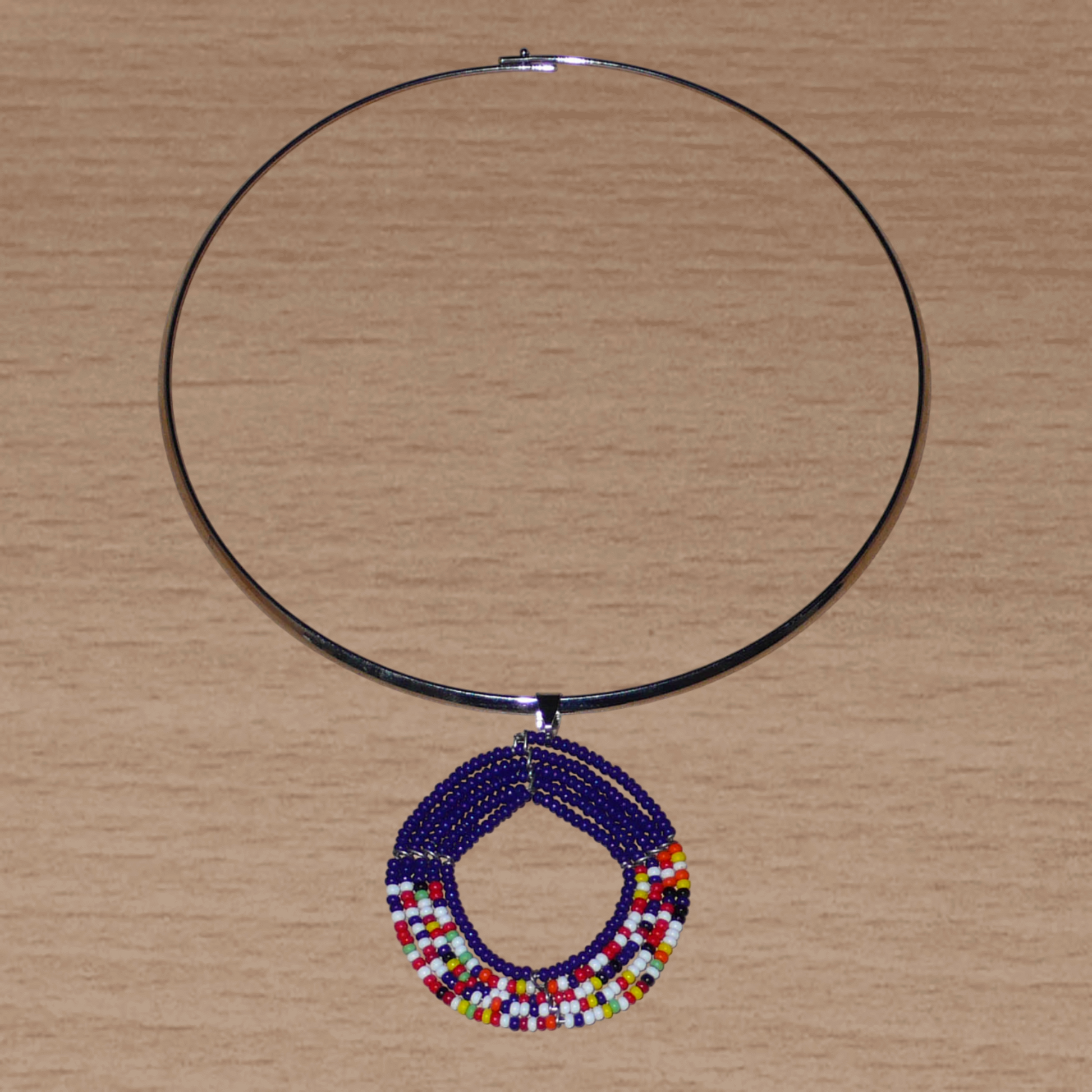 Bijou ethnique afro chic composé d'un collier ras de cou en laiton orné d'un médaillon Massai fait de perles de rocaille bleu foncé et multicolores.