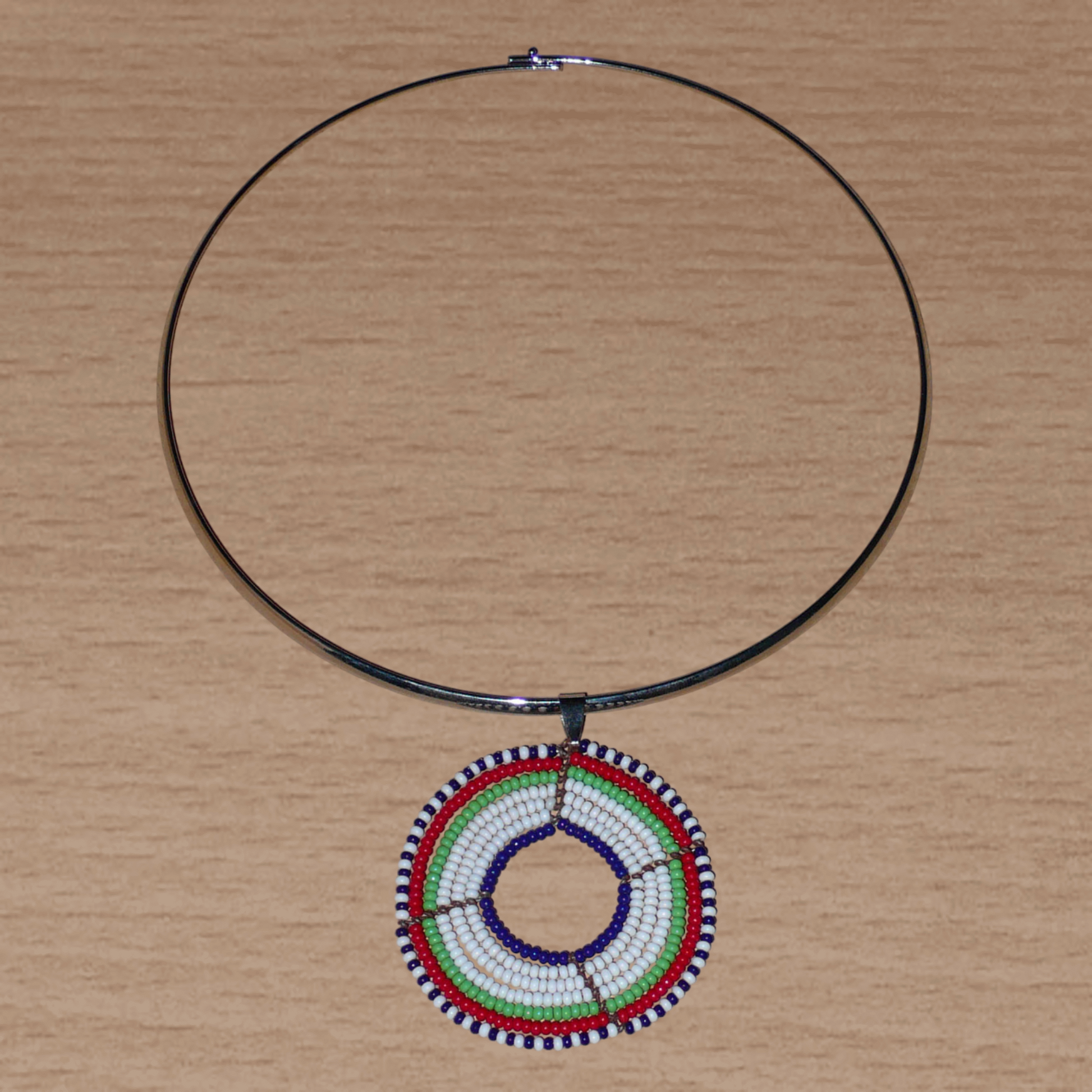 Collier ethnique contemporain composé d'un ras de cou en laiton orné d'un médaillon Massai fait de perles de rocaille blanches, vertes, rouges, bleu marine et noires.