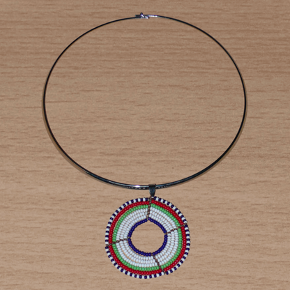 Collier ethnique contemporain composé d'un ras de cou en laiton orné d'un médaillon Massai fait de perles de rocaille blanches, vertes, rouges, bleu marine et noires.