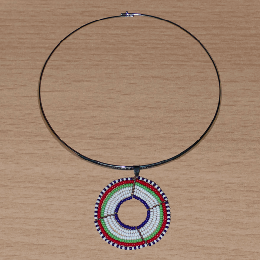Collier ethnique contemporain composé d'un ras de cou en laiton orné d'un médaillon Massai fait de perles de rocaille blanches, vertes, rouges, bleu marine et noires.