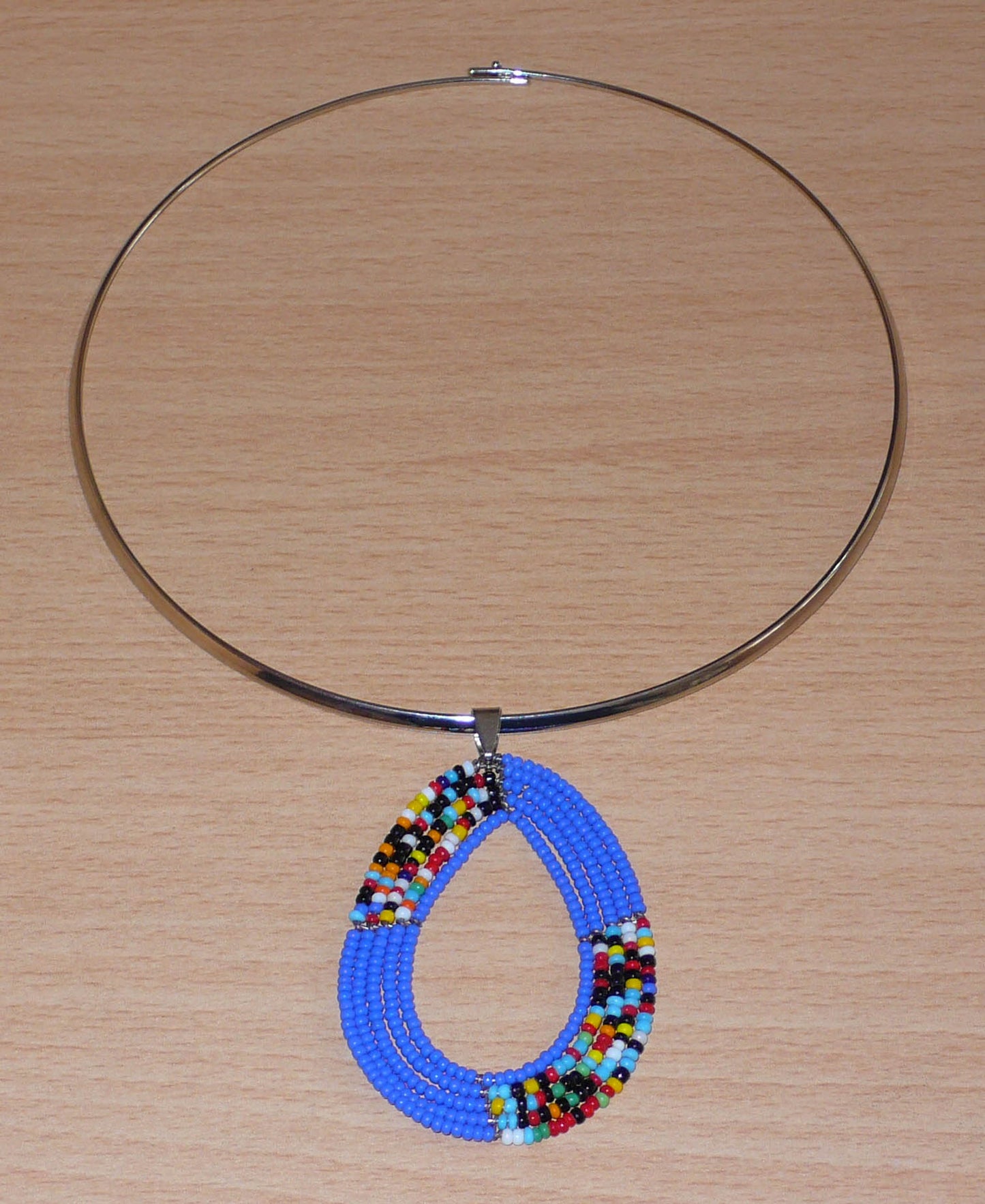 Collier ethnique composé d'un ras de cou en laiton agrémenté d'un pendentif en forme de goutte composé de perles de rocaille bleues et multicolores.