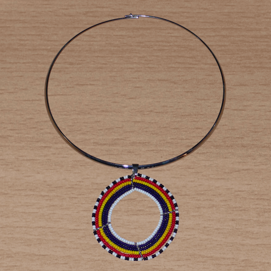 Bijou ethnique au style contemporain composé d'un ras de cou en laiton agrémenté d'un large médaillon Massai fait de perles de rocaille bleu foncé, rouges, jaunes, blanches et noires.