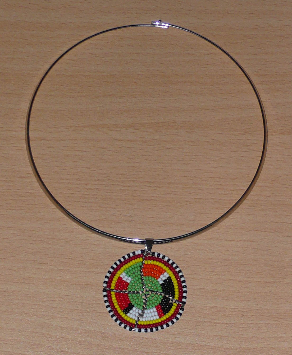 Bijou africain contemporain composé d'un collier ras de cou en laiton rehaussé d'un médaillon à motifs ethniques Massai fait d'un tissage de perles vertes et multicolores.