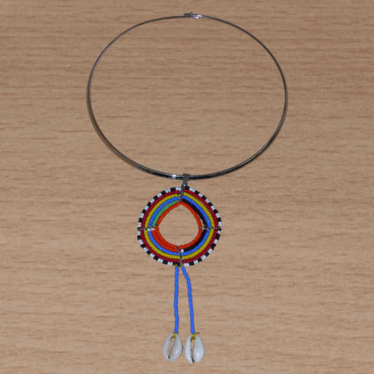 Collier ethnique de style afro bohème composé d'un ras de cou en laiton orné d'un long pendentif Massai fait de perles de rocaille et de coquillages cauris.