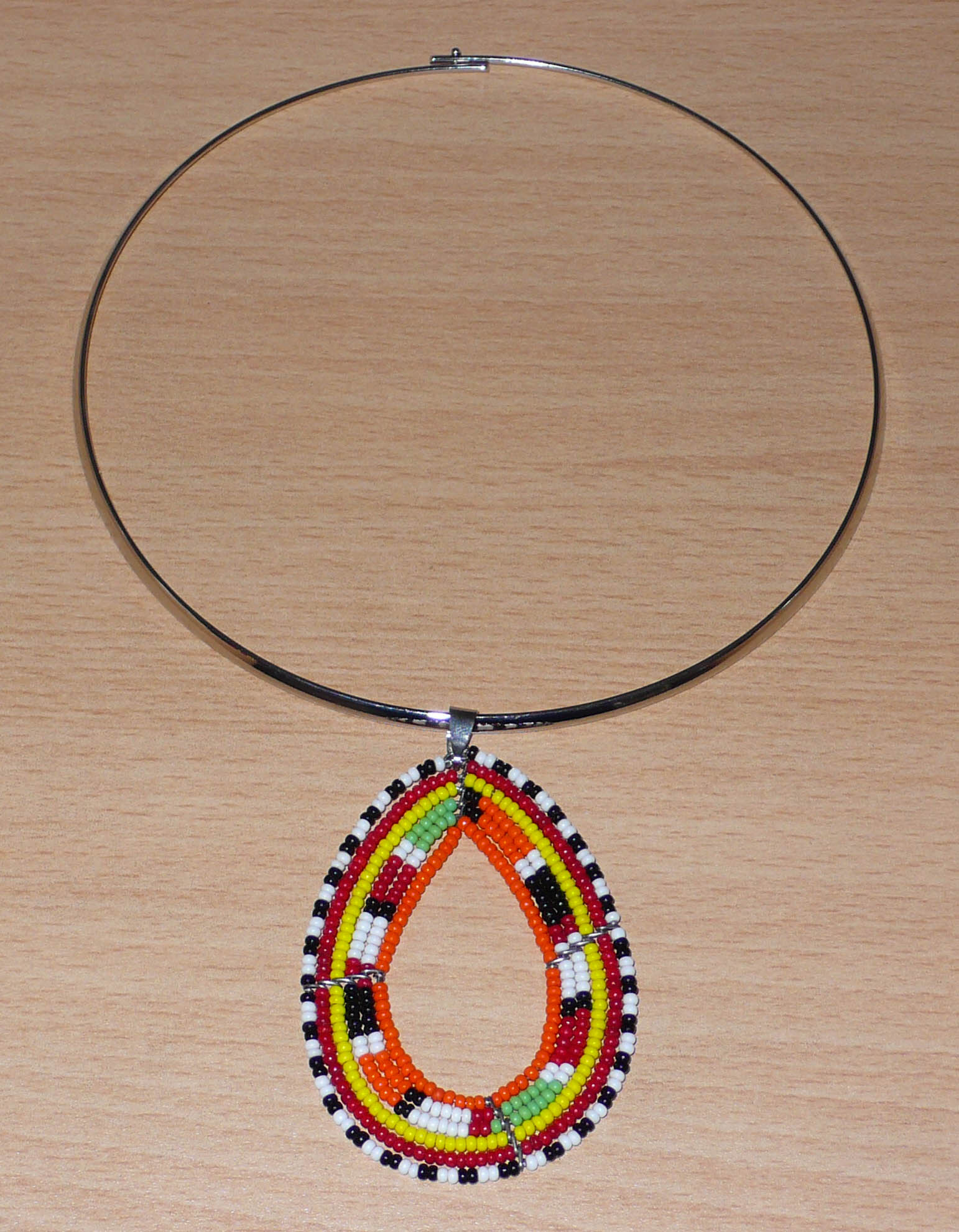 Collier africain composé d'un ras de cou en laiton décoré d'un long et large pendentif en forme de goutte et à motifs ethniques Massai fait de perles de rocaille.