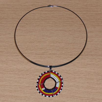 Collier ethnique contemporain se composant d'un ras de cou en laiton orné d'un pendentif rond à motifs Massai fait d'un tissage de perles de rocaille rouges, blanches, bleues, jaunes, noires et blanches.