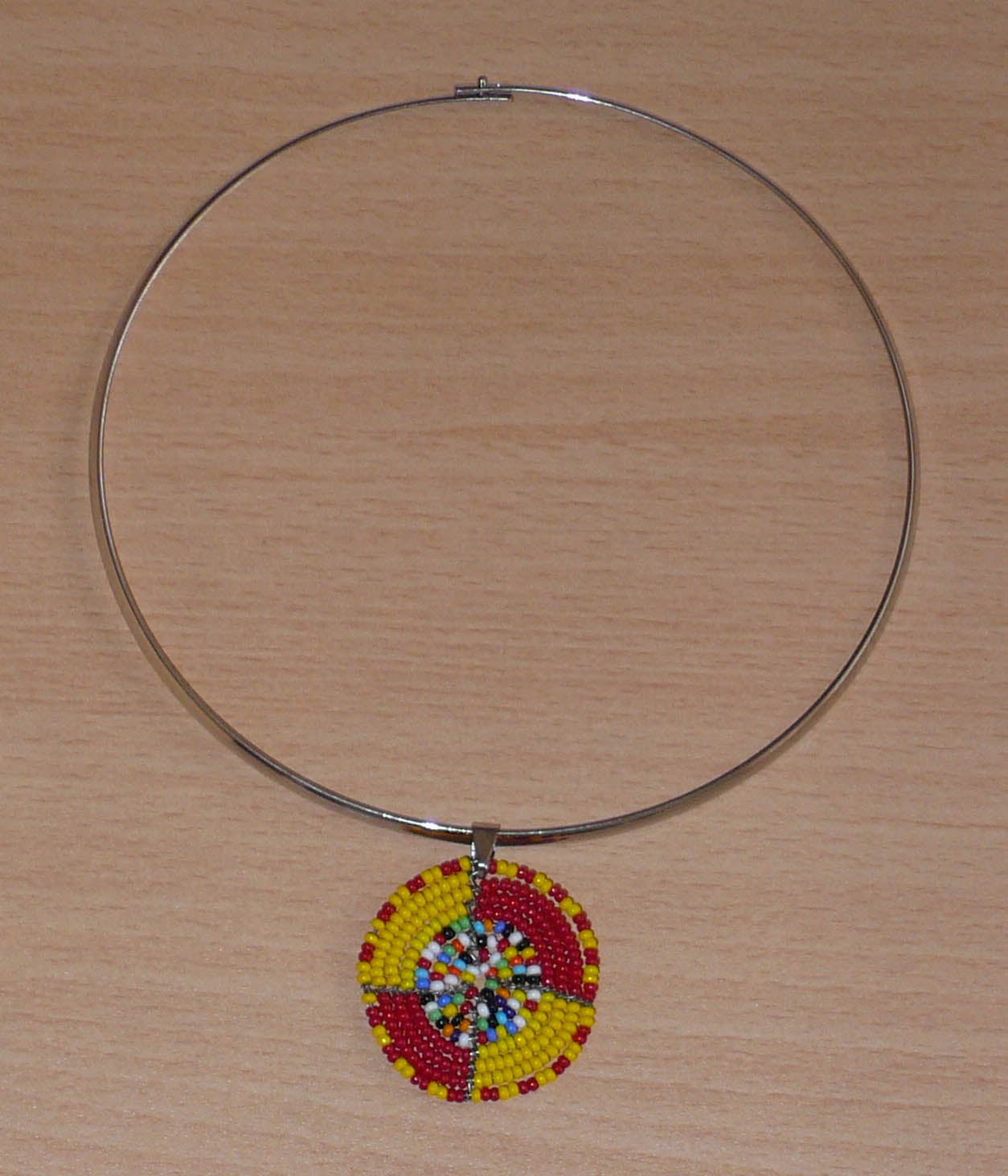 Collier ethnique composé d'un ras de cou en laiton rehaussé d'un petit médaillon Massai en perles de rocaille rouges, jaunes et multicolores.