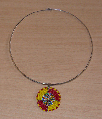 Collier ethnique composé d'un ras de cou en laiton rehaussé d'un petit médaillon Massai en perles de rocaille rouges, jaunes et multicolores.